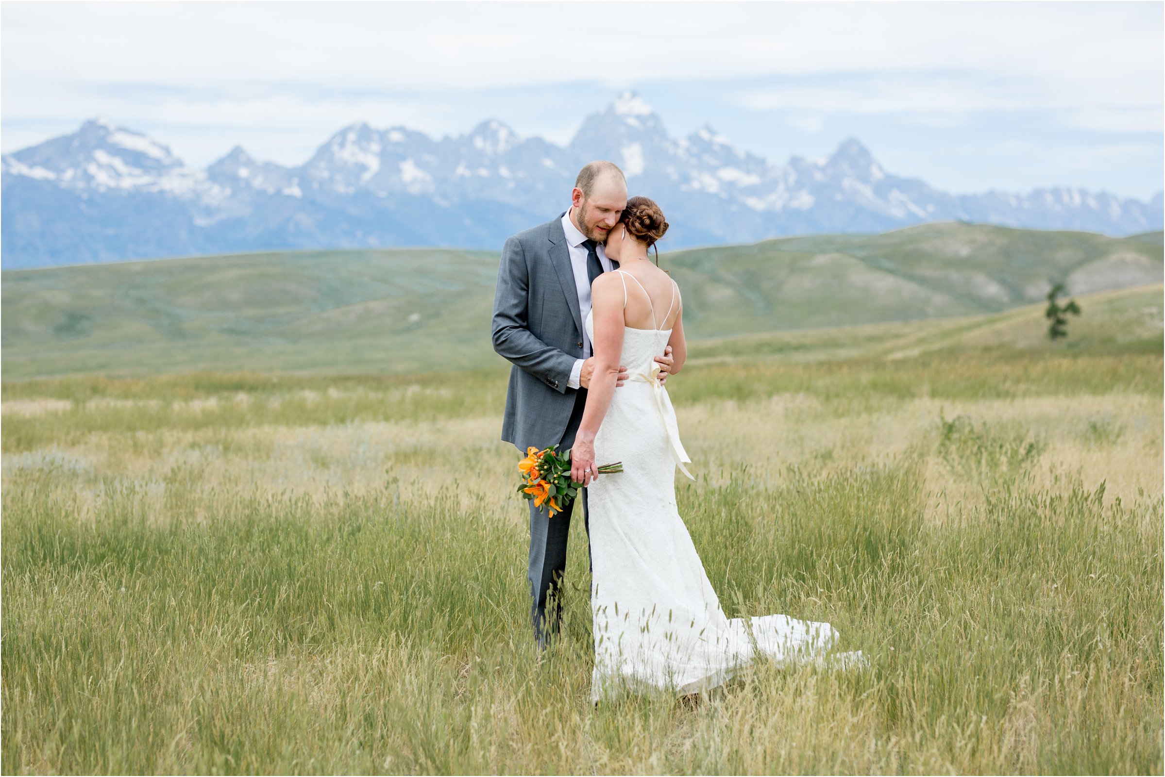 bride and groom snuggle in a field with the tetons in the background