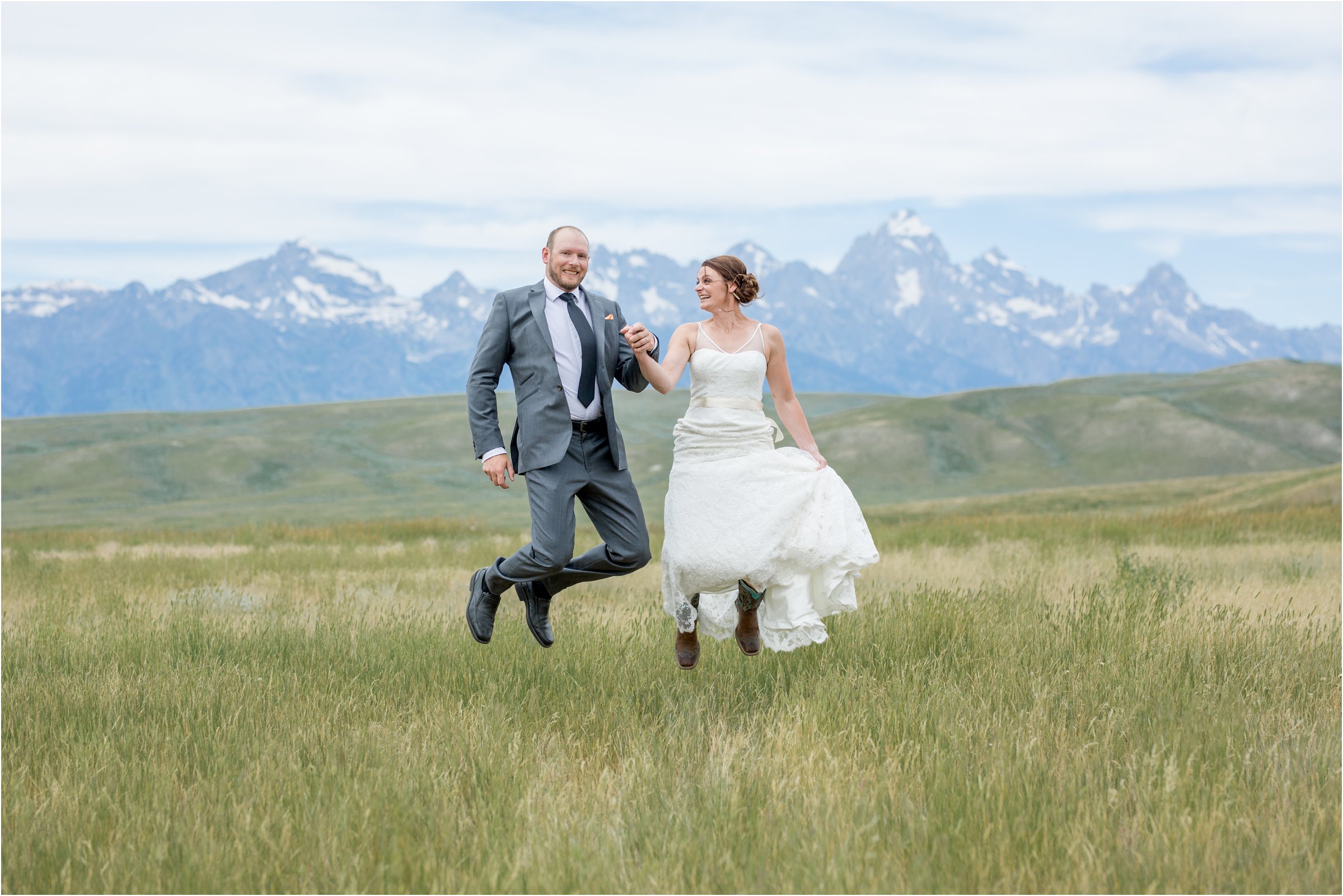 bride and groom jump together in tall grass in front of the tetons