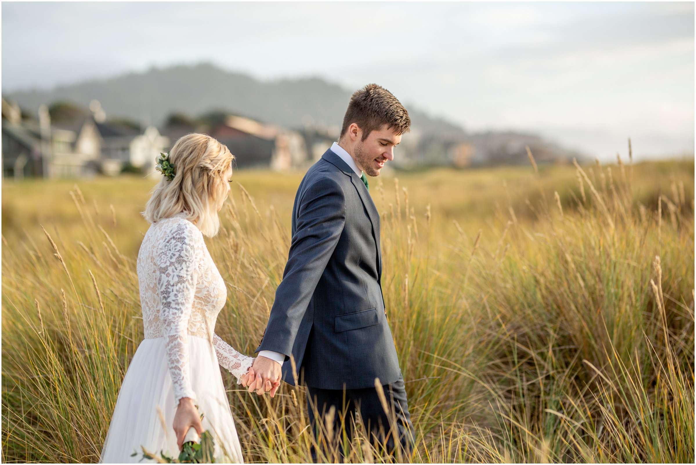 Bride and groom walk through tall grass headed toward the beach after their wedding