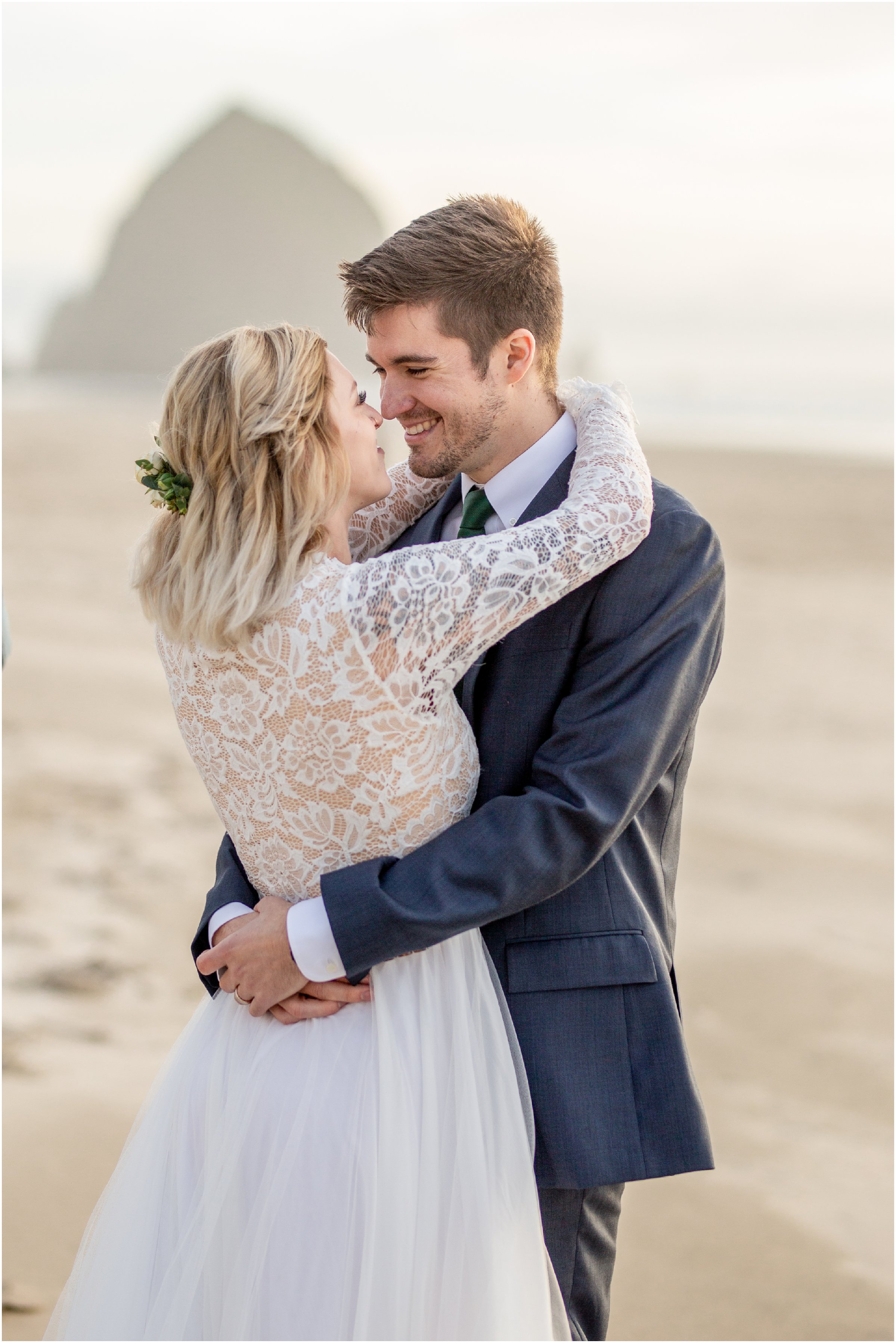 bride and groom snuggle on the beach with haystack rock in the background
