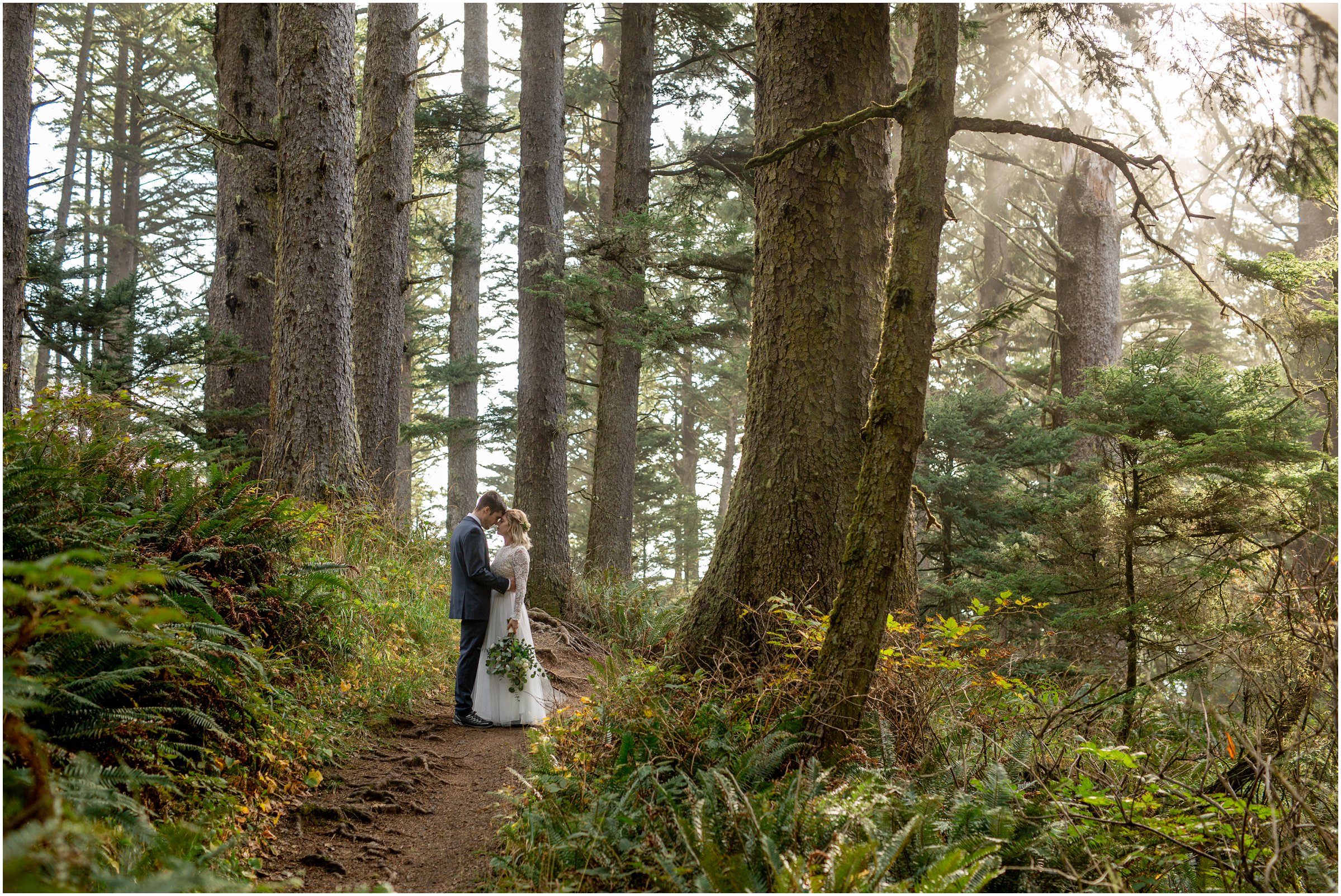bride and groom snuggle on a path in ecola state park with large trees surrounding them