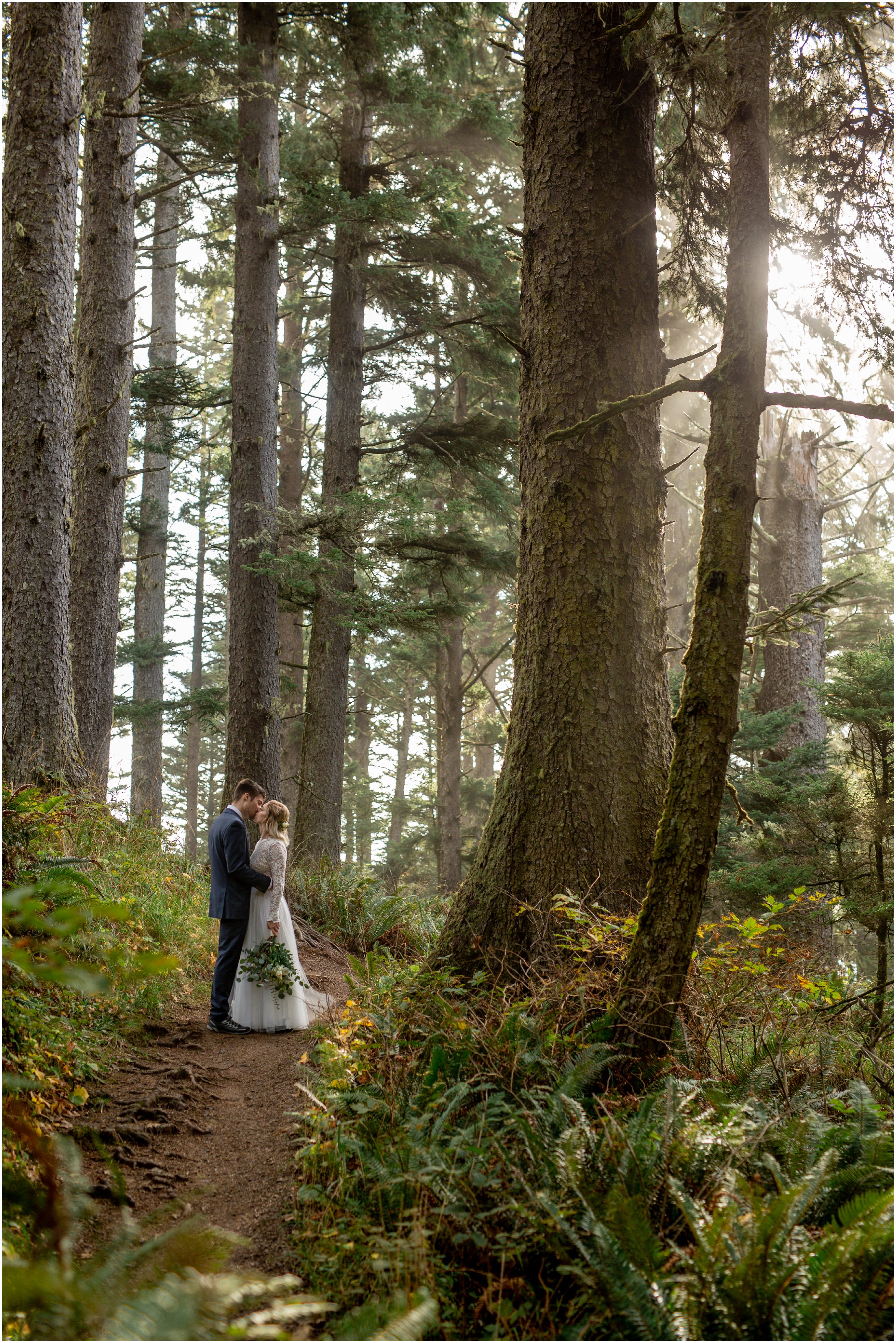 bride and groom snuggle on a path in ecola state park with large trees surrounding them
