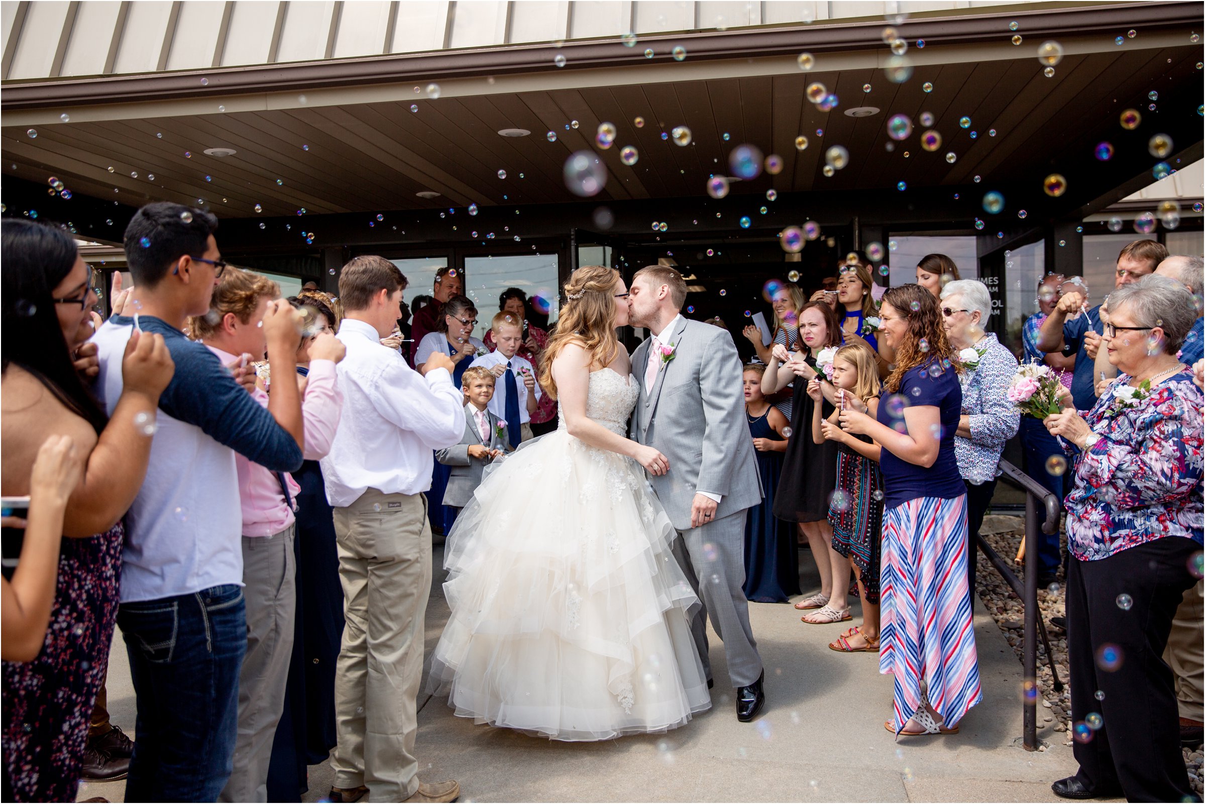 bride and groom exit their ceremony surrounded with bubbles after their holdrege trinity church wedding