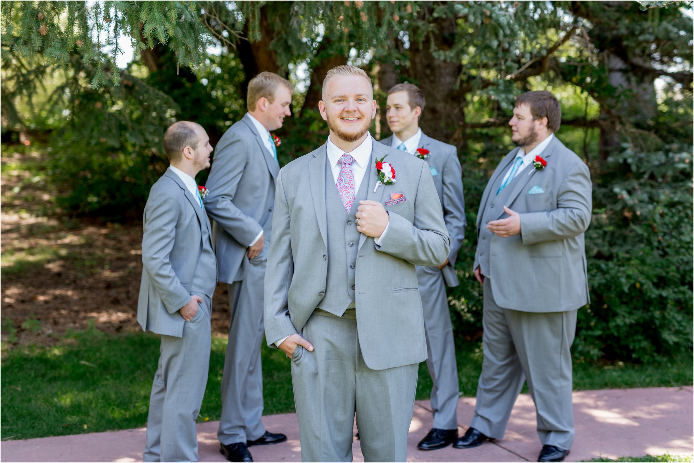 groom poses with his groomsmen in gray tuxedos with blue ties and red flowers