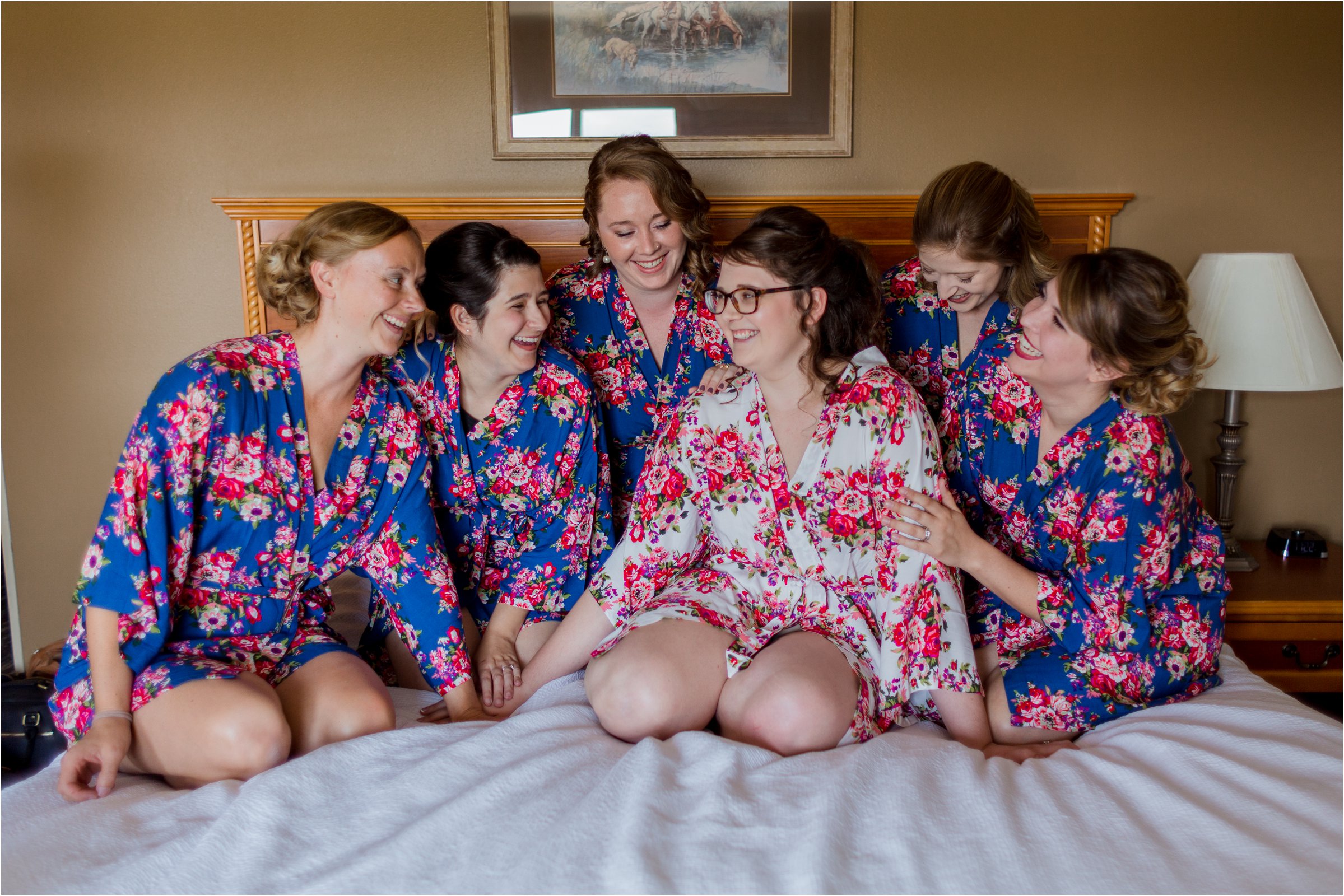 bride and bridesmaids pose on a hotel bed in their floral robes before getting into her wedding dress