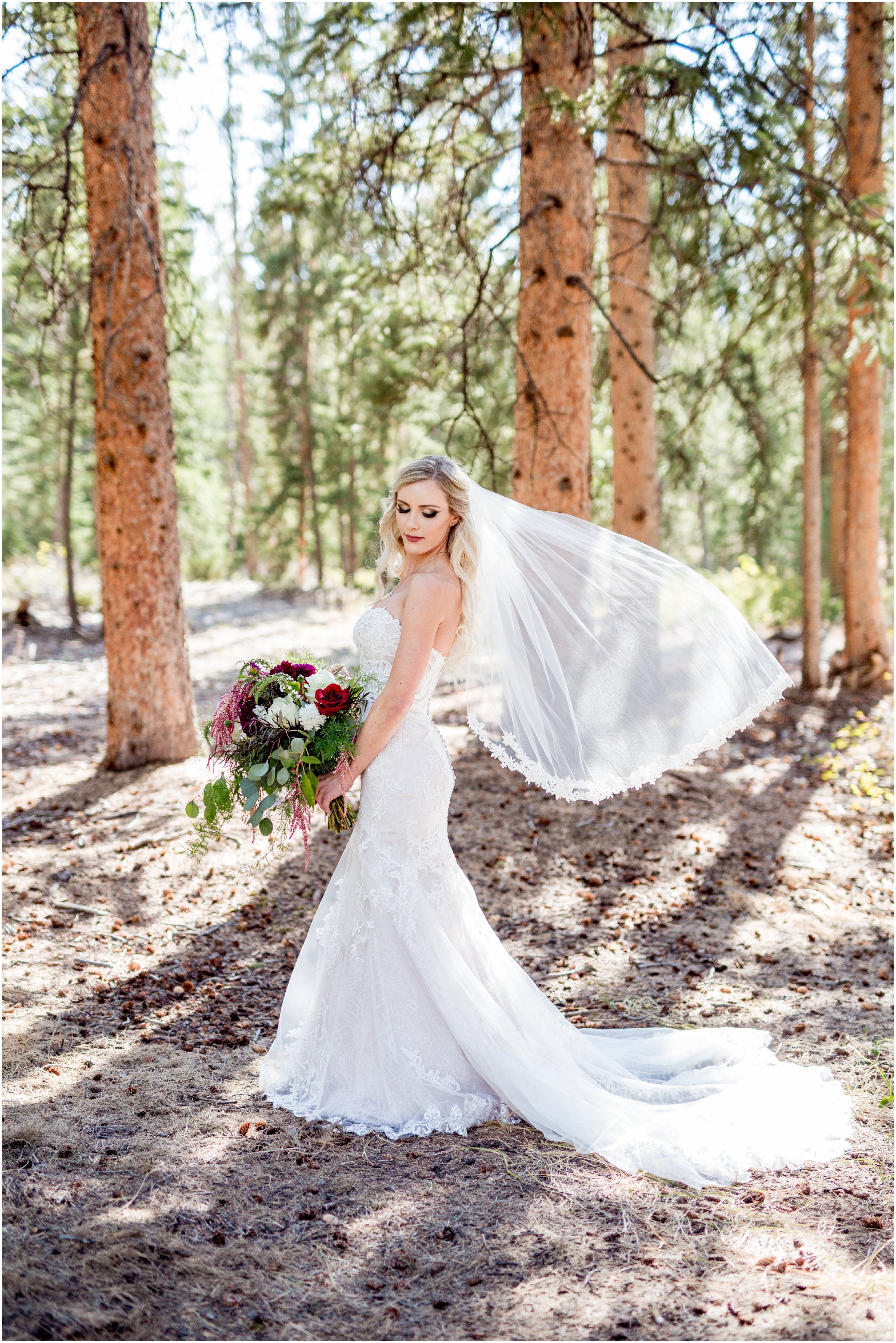 bride standing alone in front of trees with veil blowing out behind her