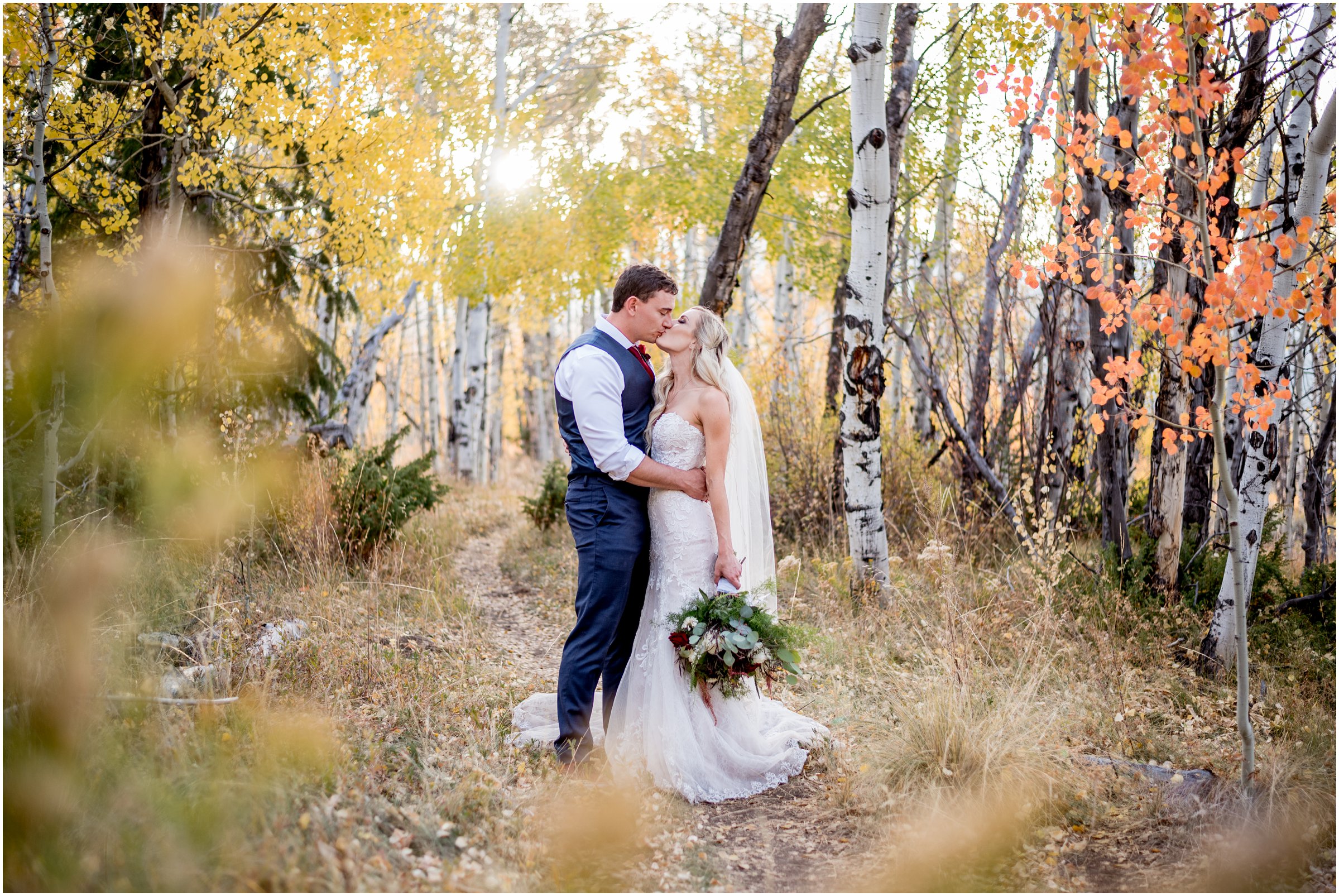 bride and groom in an aspen grove kissing with a large bouquet held downward