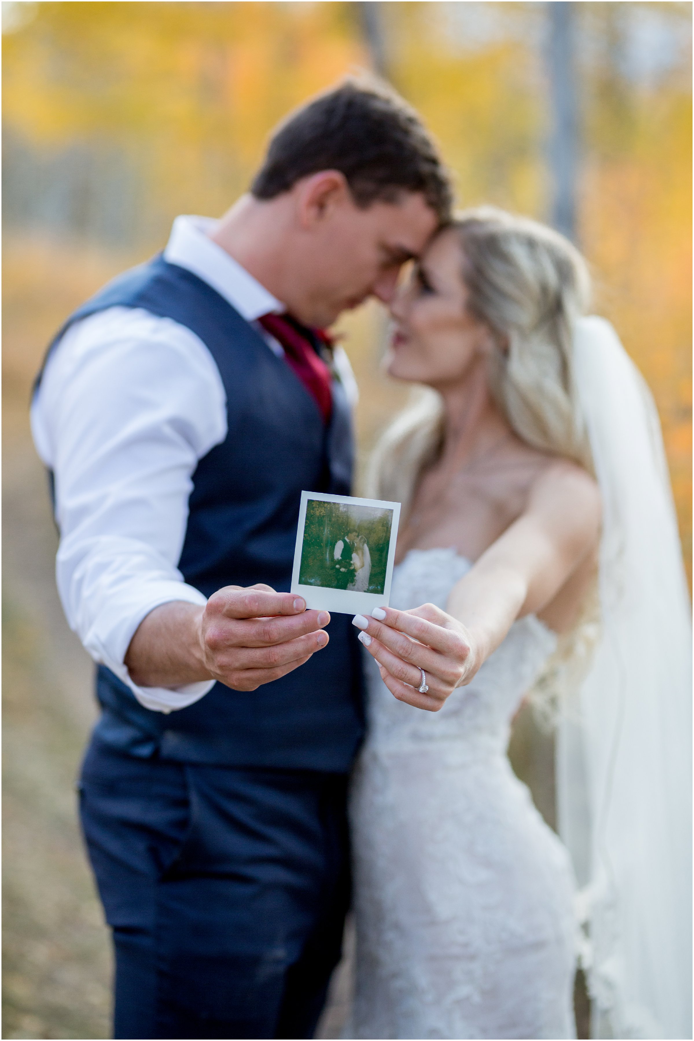 bride and groom hold a vintage polaroid picture out while they stand face to face