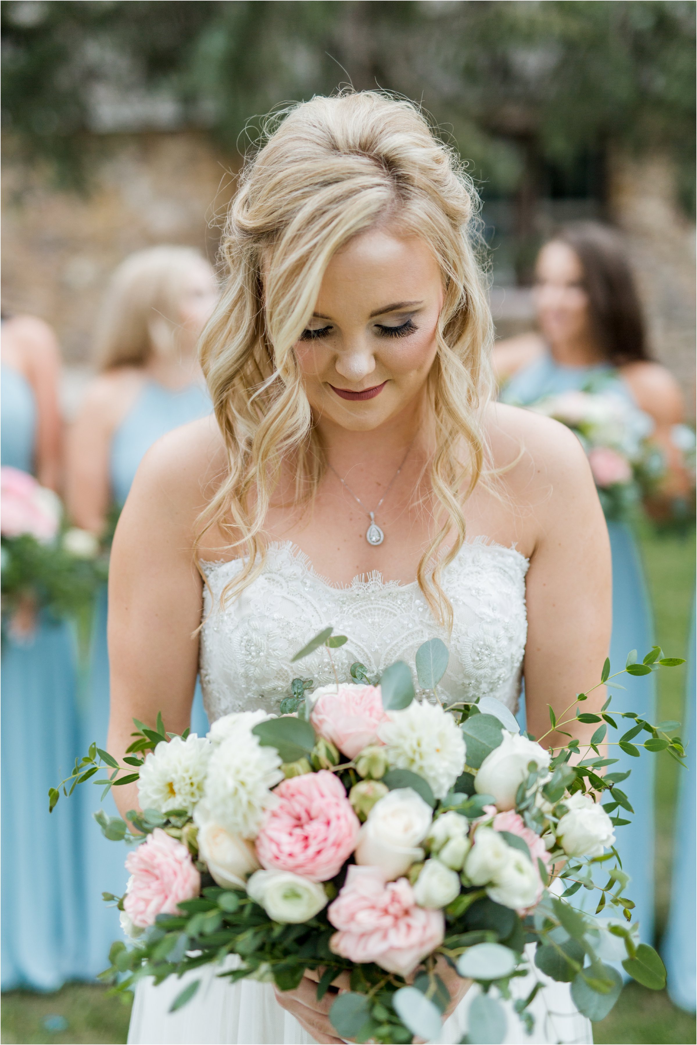 the bride looking down at her bouquet as her bridesmaids stand in the background in blue