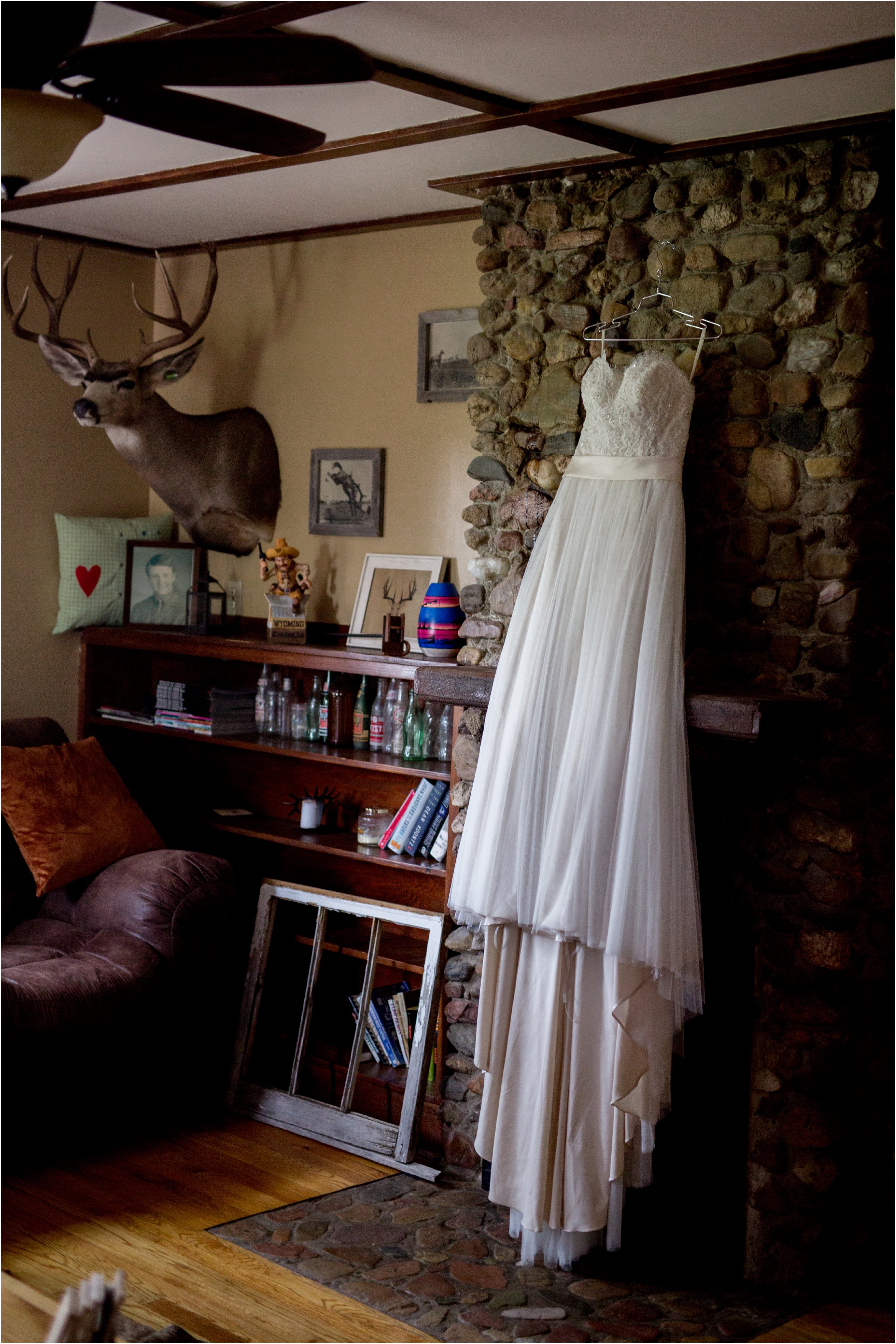 the bride's wedding dress hanging in their living room on the historic stone fireplace