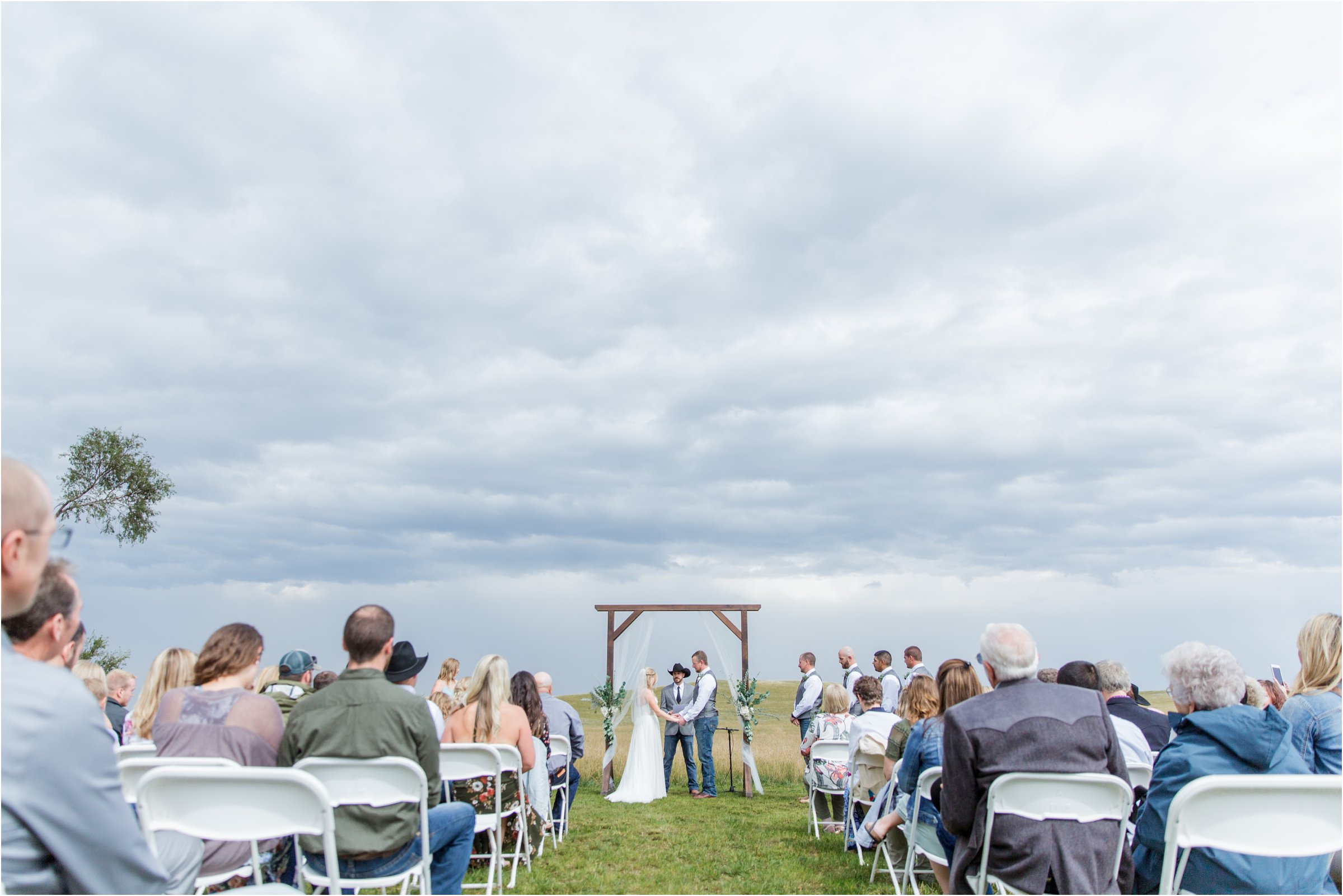the bride and groom hold hands in front of their guests for the ceremony on the wyoming prairie