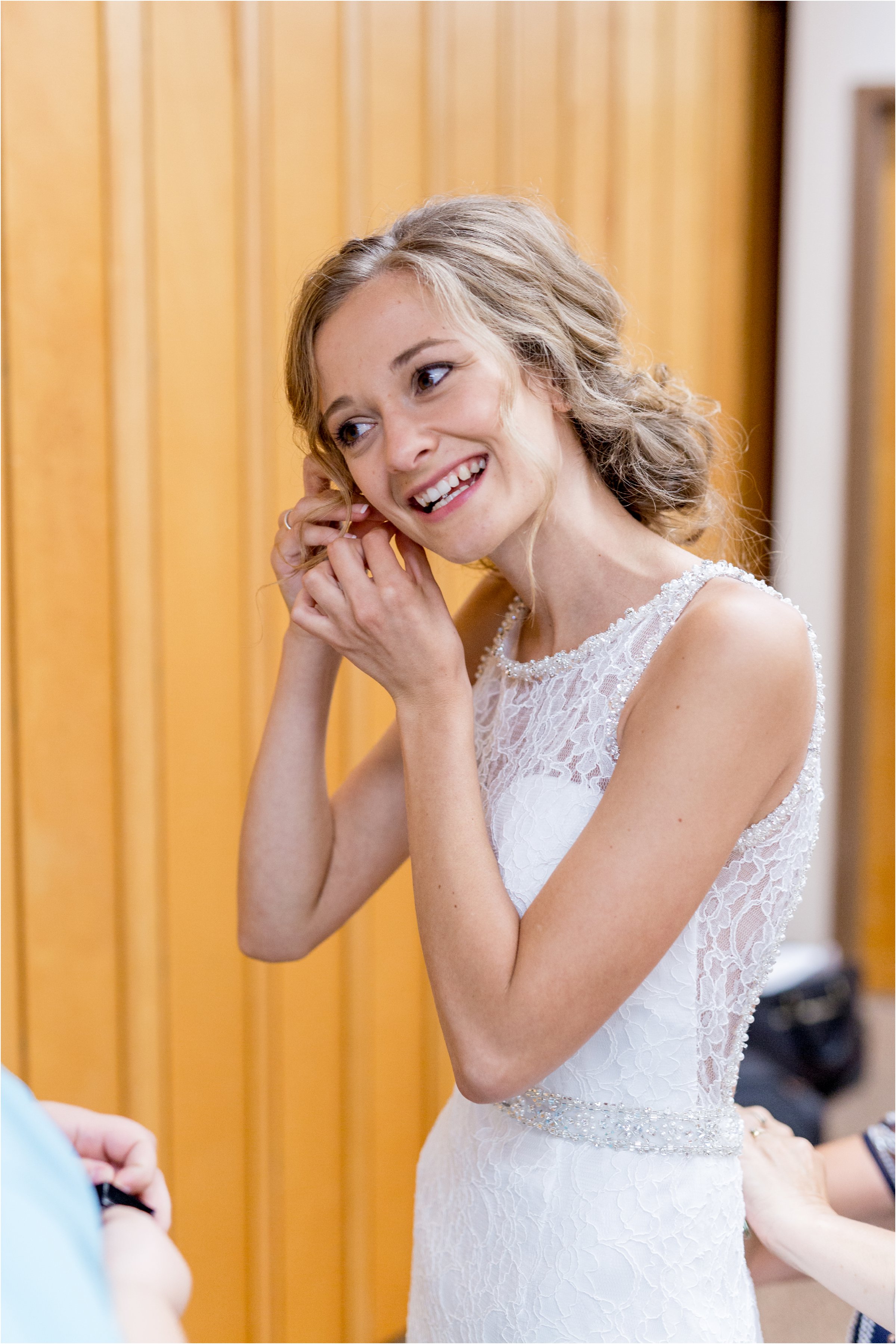 bride puts in earrings on the morning of her wedding after putting on her dress
