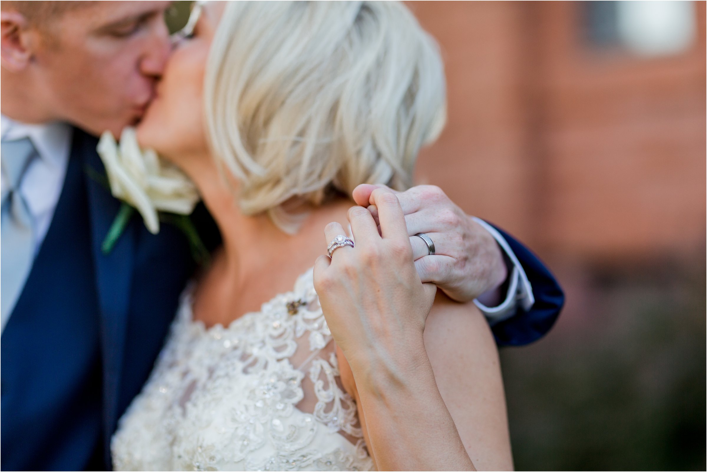 bride and groom kiss with wedding rings in foreground