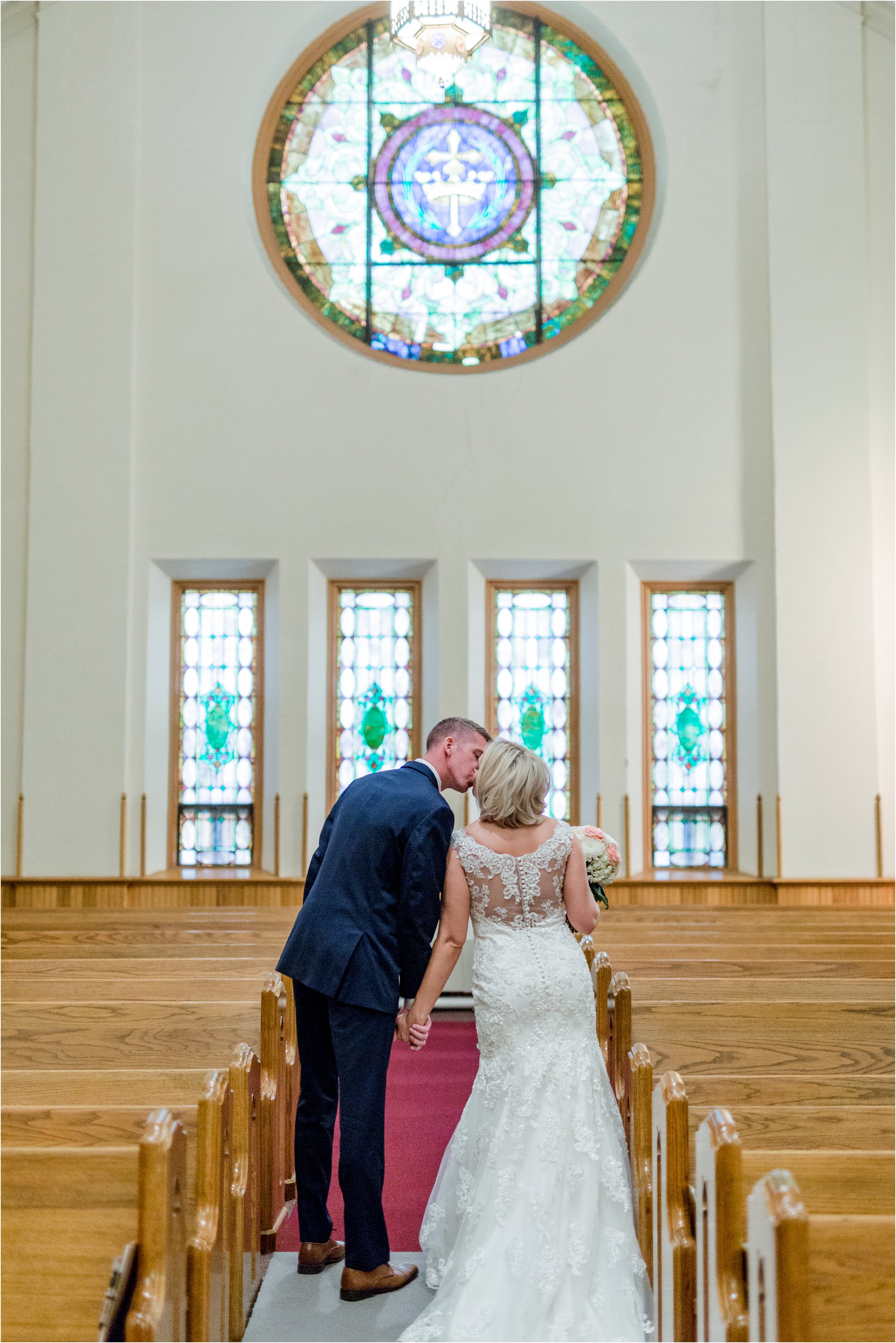 bride and groom kiss in church sanctuary with round stained glass window in the background