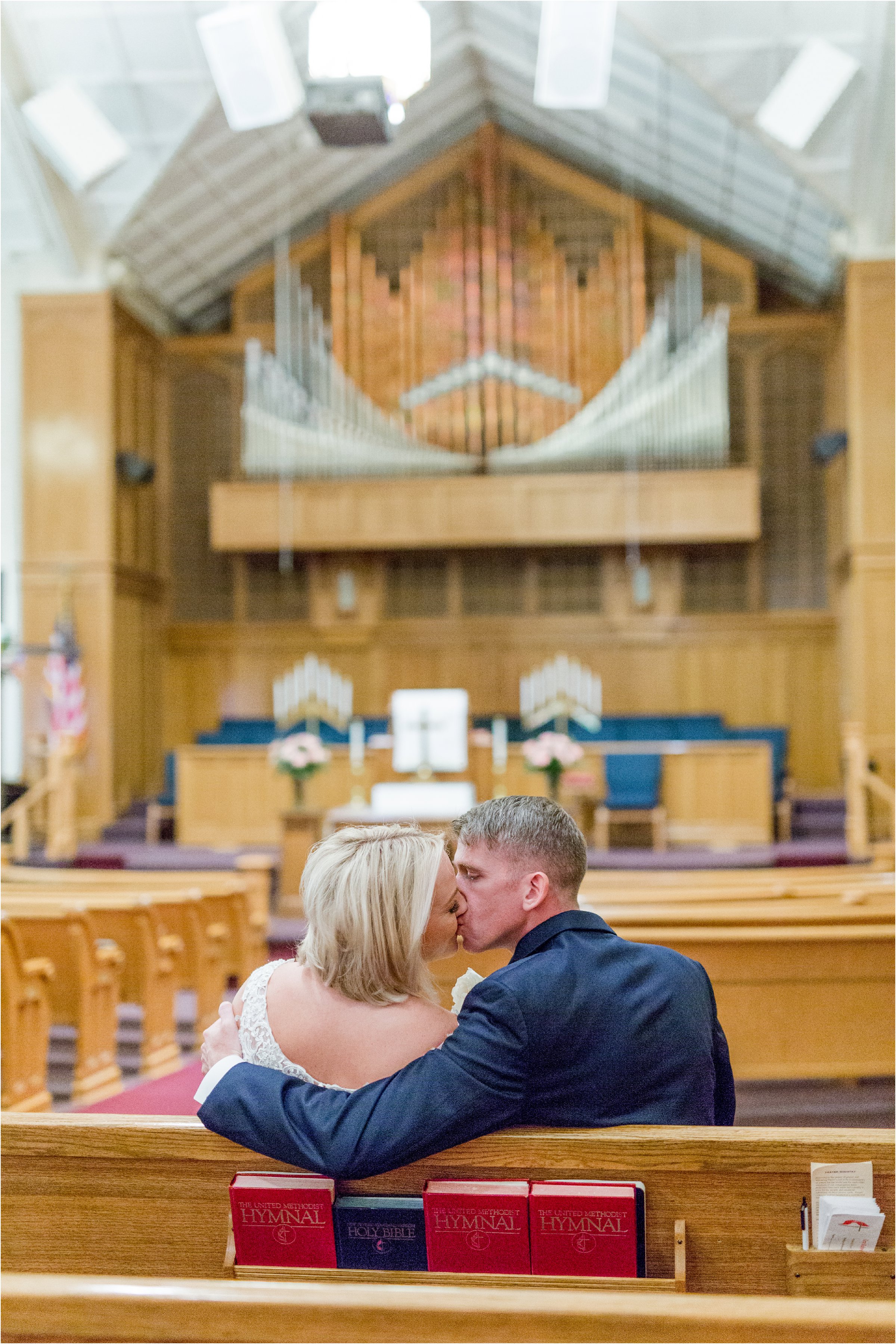 bride and groom sit in church pew kissing with sanctuary in the background