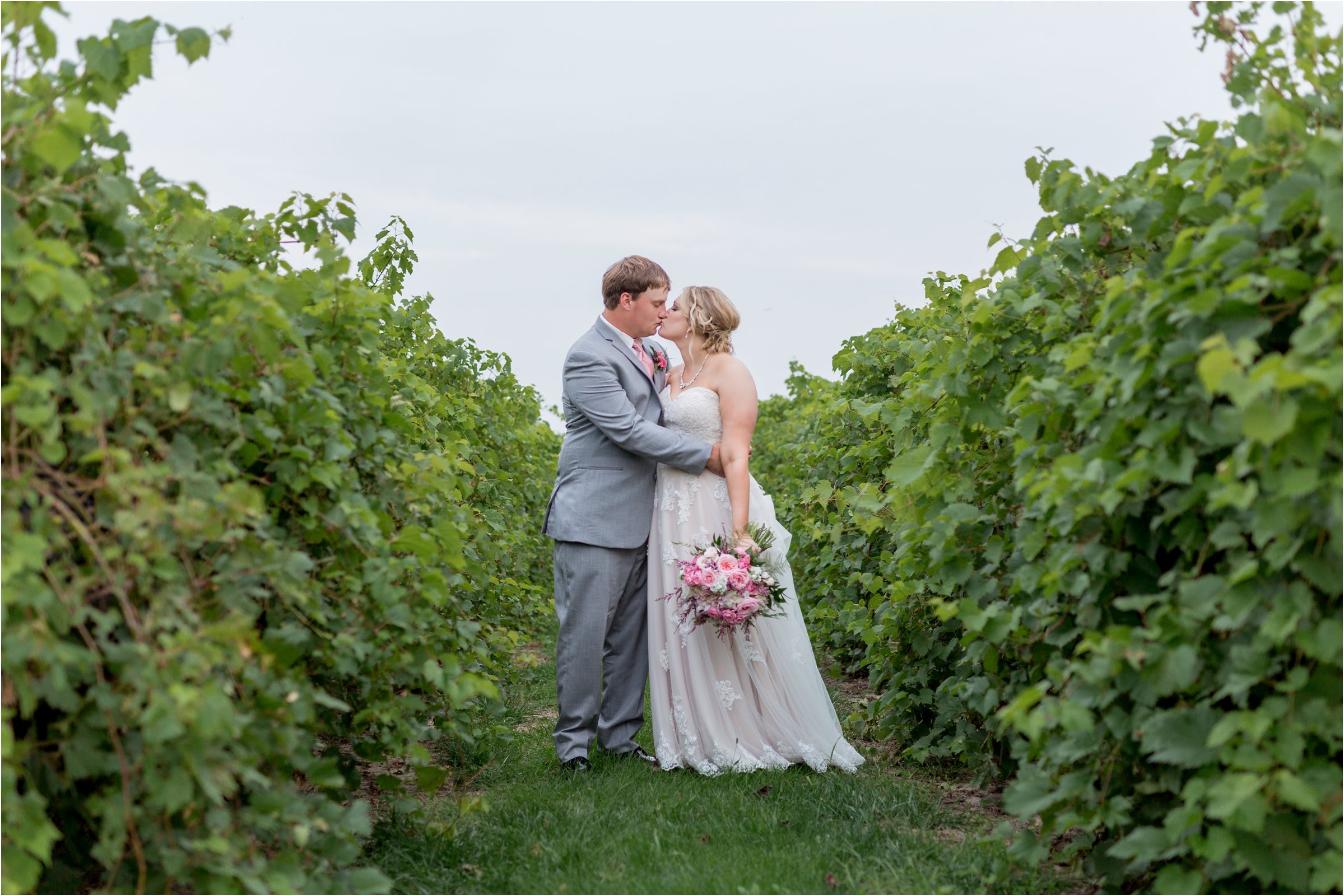 the bride and groom snuggle together in between grape vines with the bride's large bouquet