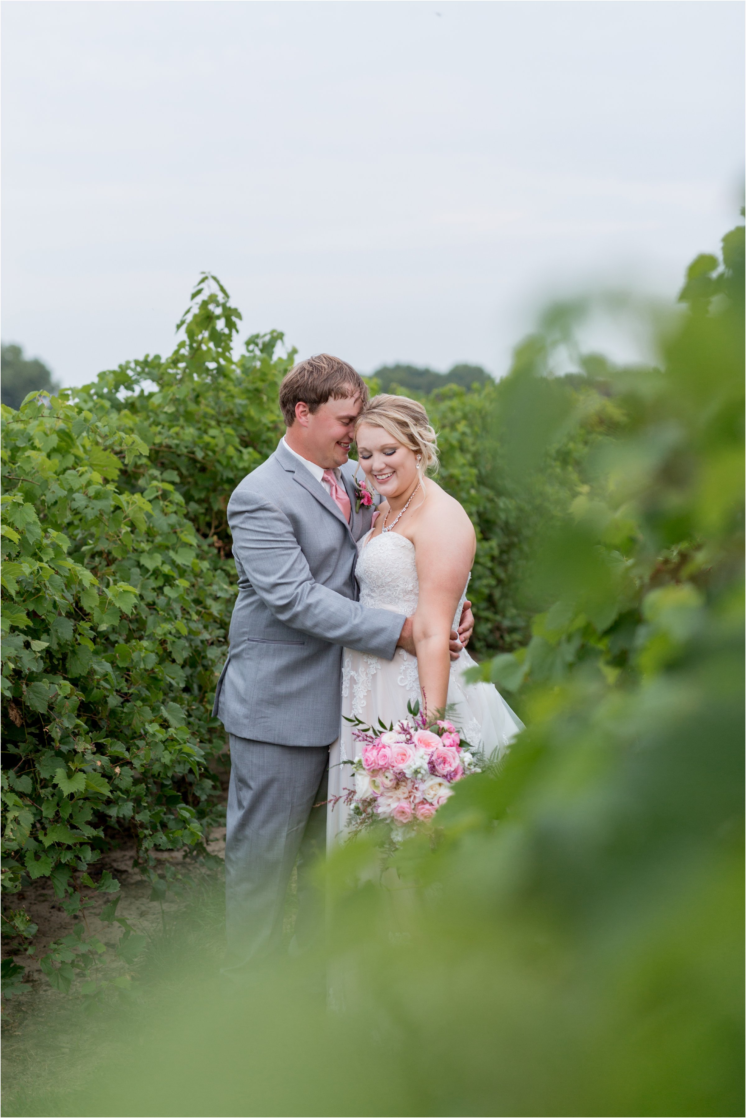 the bride and groom snuggle together in between grape vines with the bride's large bouquet