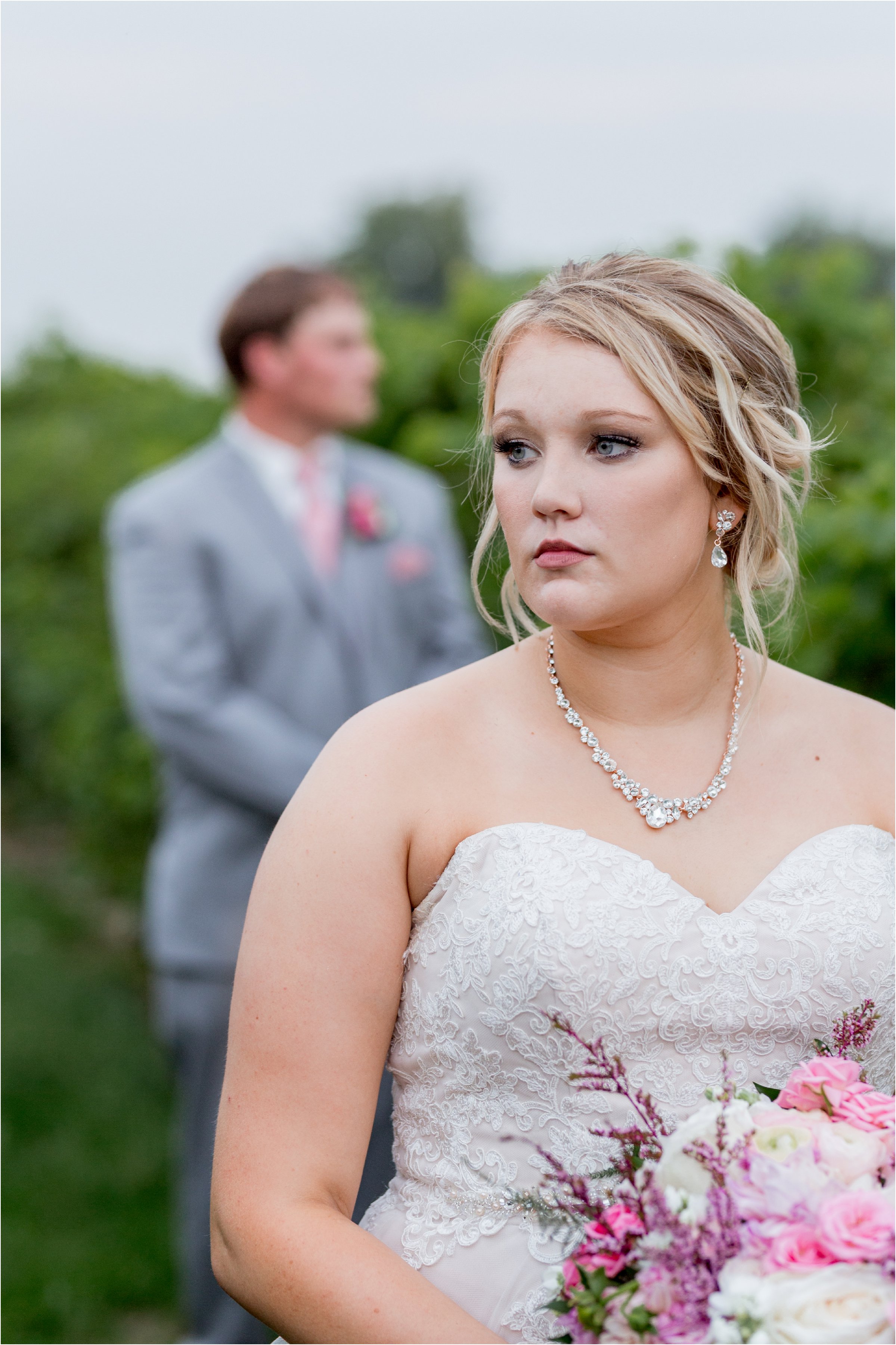 the bride in the foreground looking off to the left while the groom in the background looks off to the right