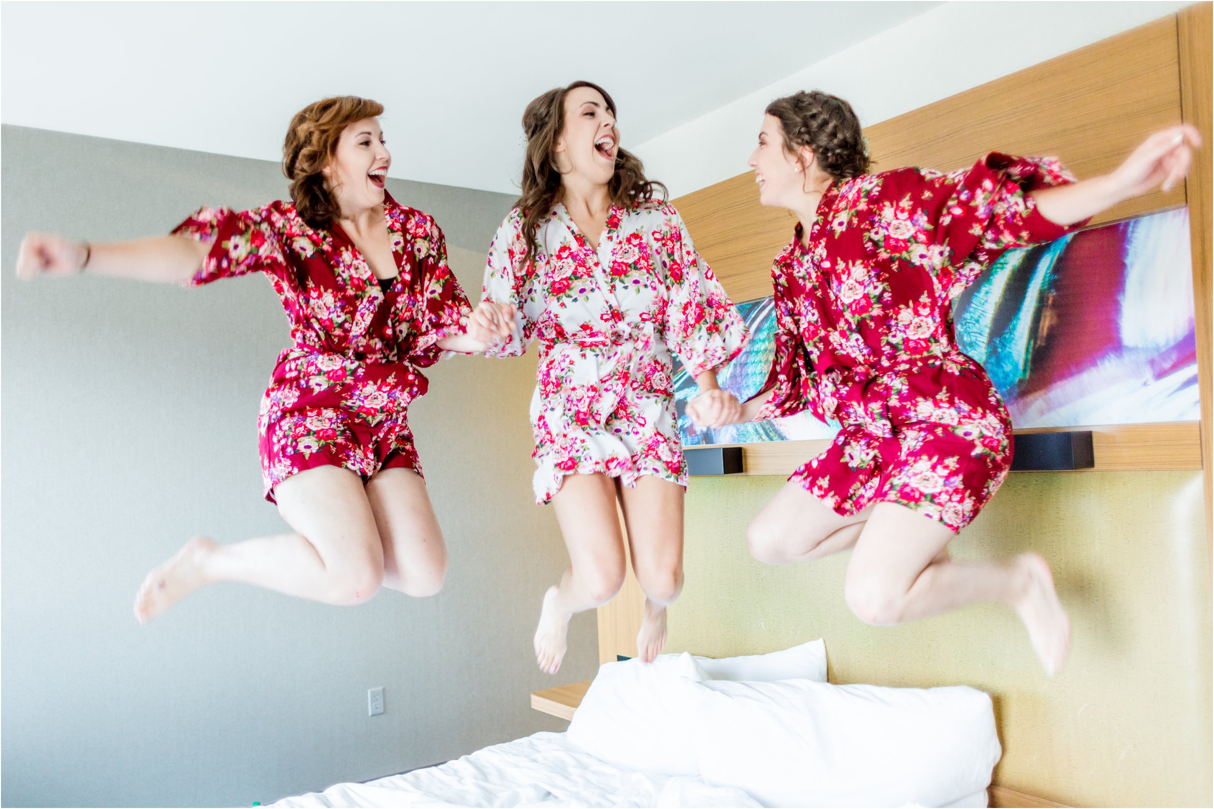 bride and sisters jump on bed together before getting ready for her wedding day