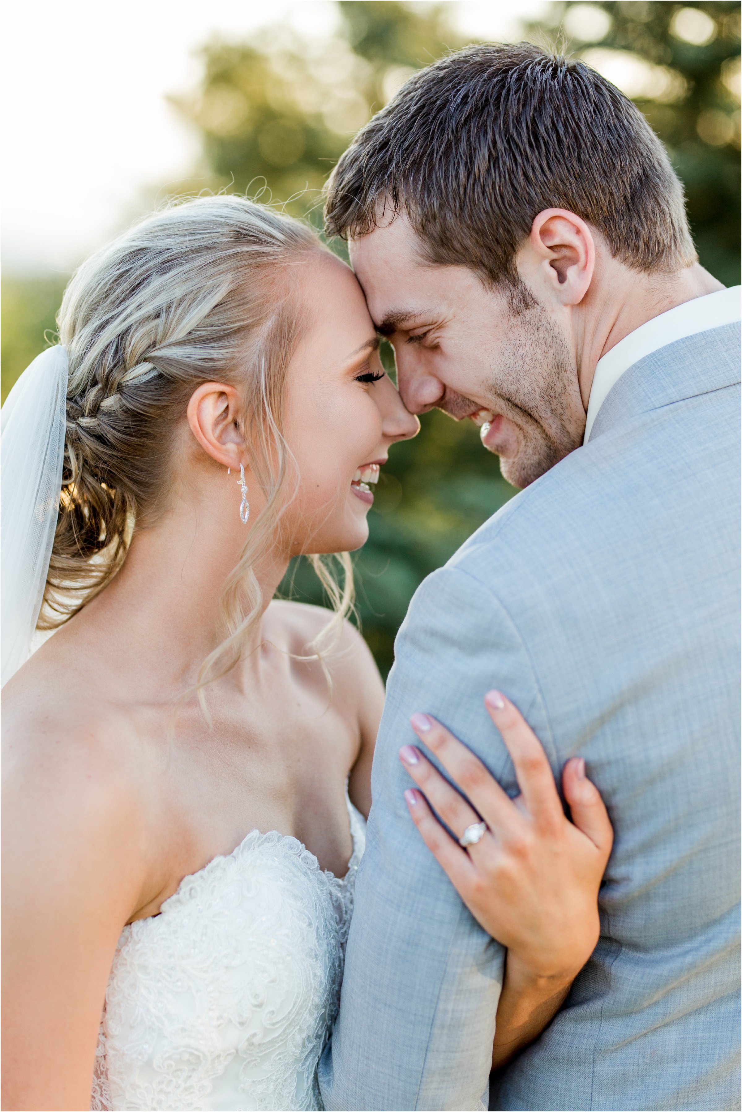 bride and groom put their foreheads together and laugh in front of sun shinging through trees