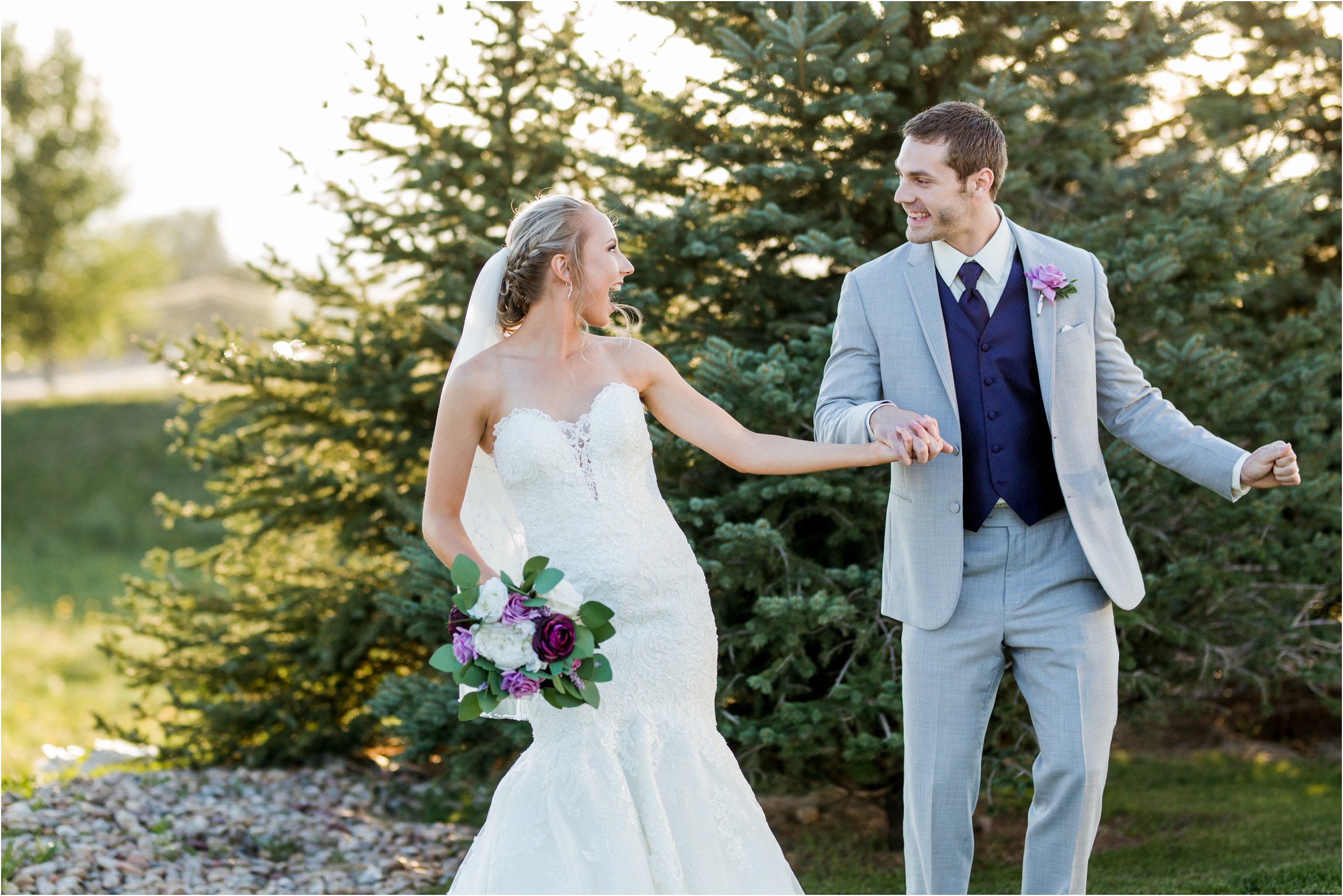 bride and groom dance together in front of trees as the golden light of sunset shines through