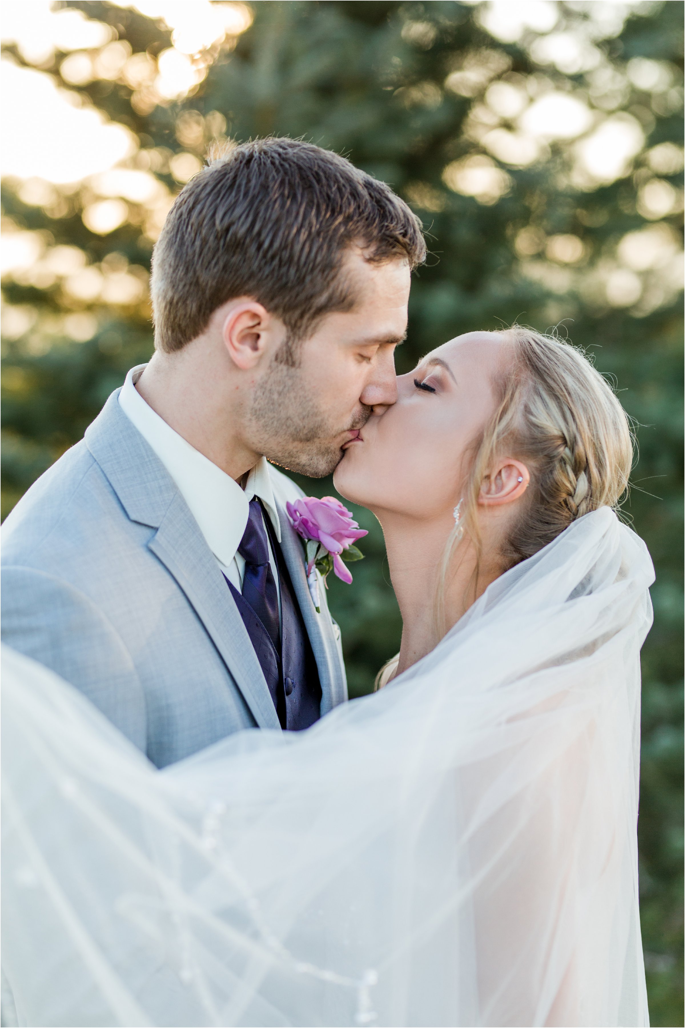 close up of bride and groom kissing in front of trees as the golden light of sunset shines through