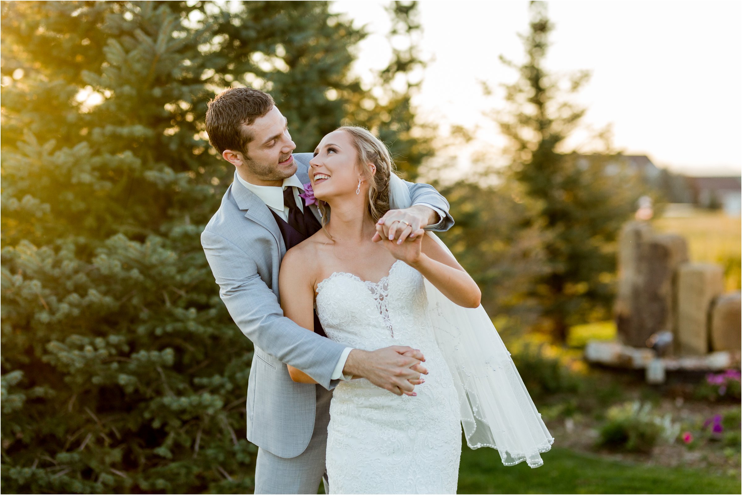 bride and groom snuggle in front of trees as the golden light of sunset shines through