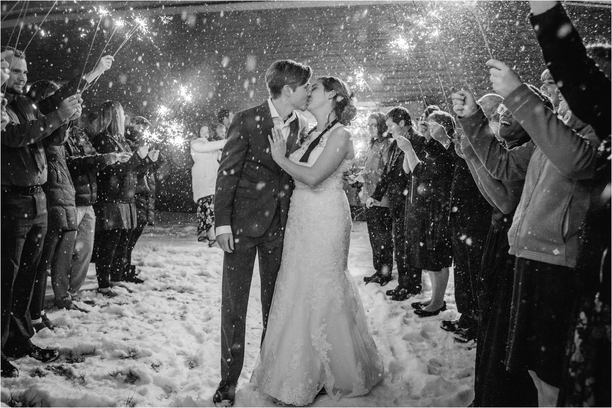 Bride and groom with sparklers above them as they head for a car in the night snow