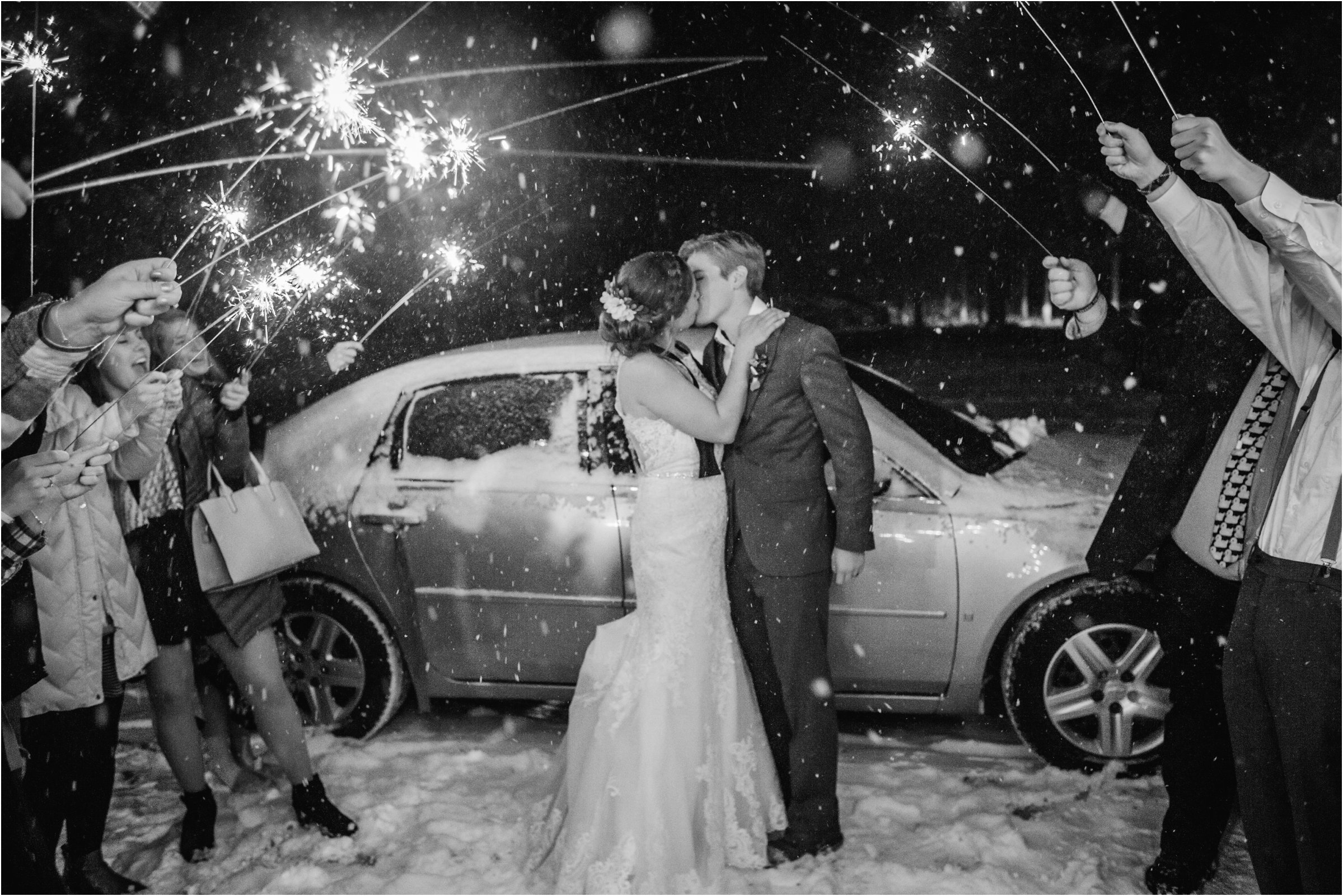Bride and groom with sparklers above them as they head for a car in the night snow