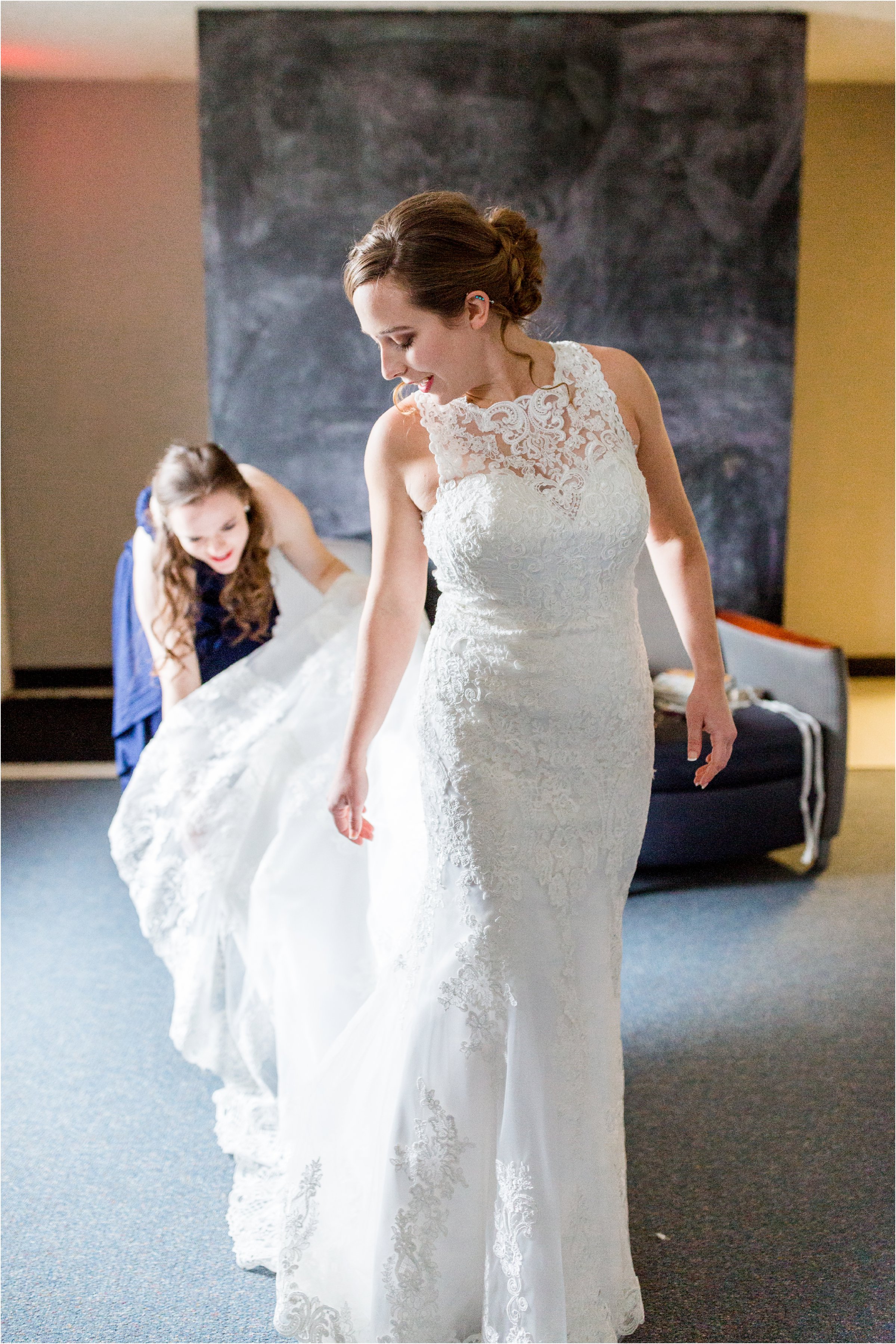 bride is helped into wedding dress by bridesmaids who button and her in and help with jewelry