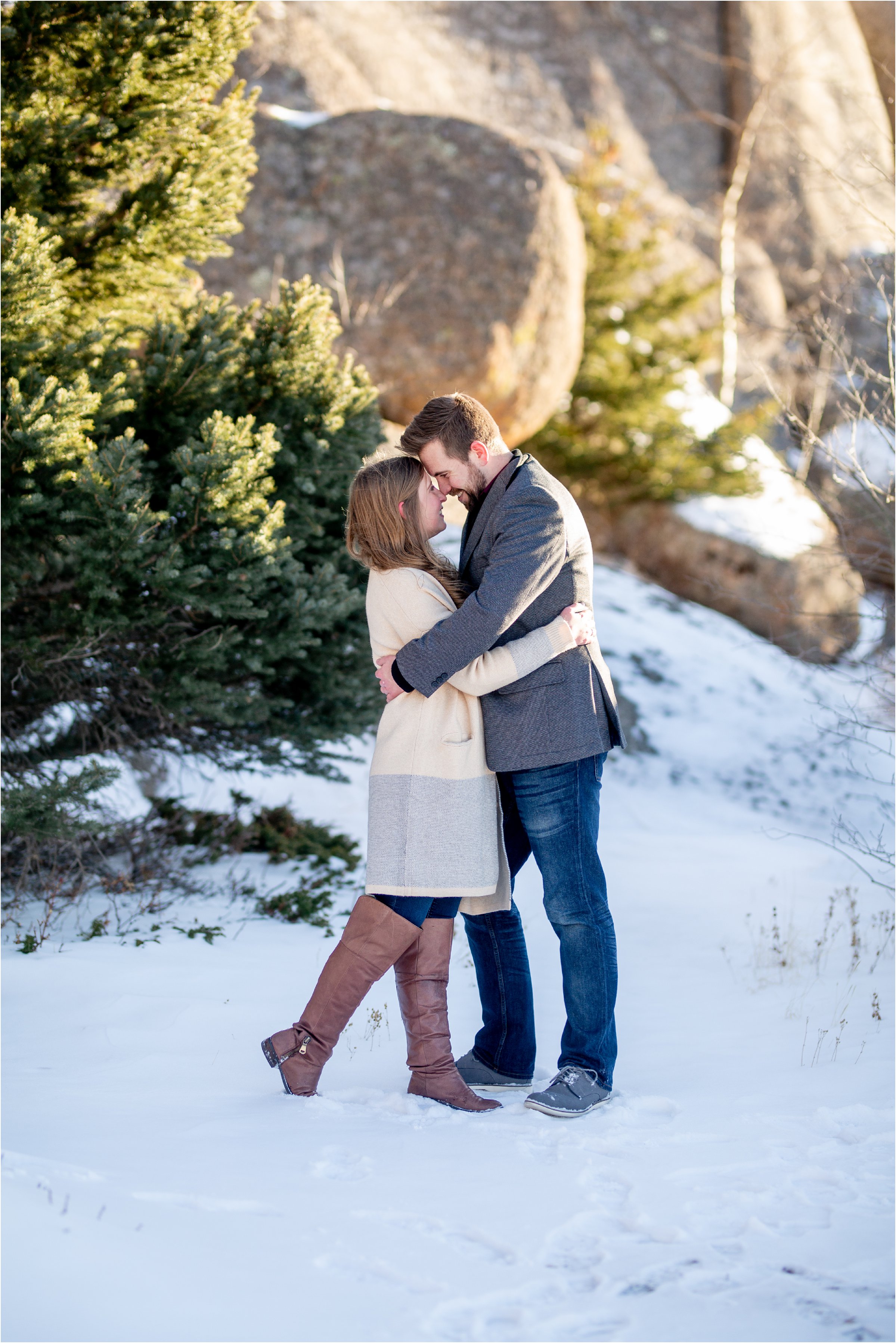 engaged couple standing face to face in the snow with rocks and trees in the background