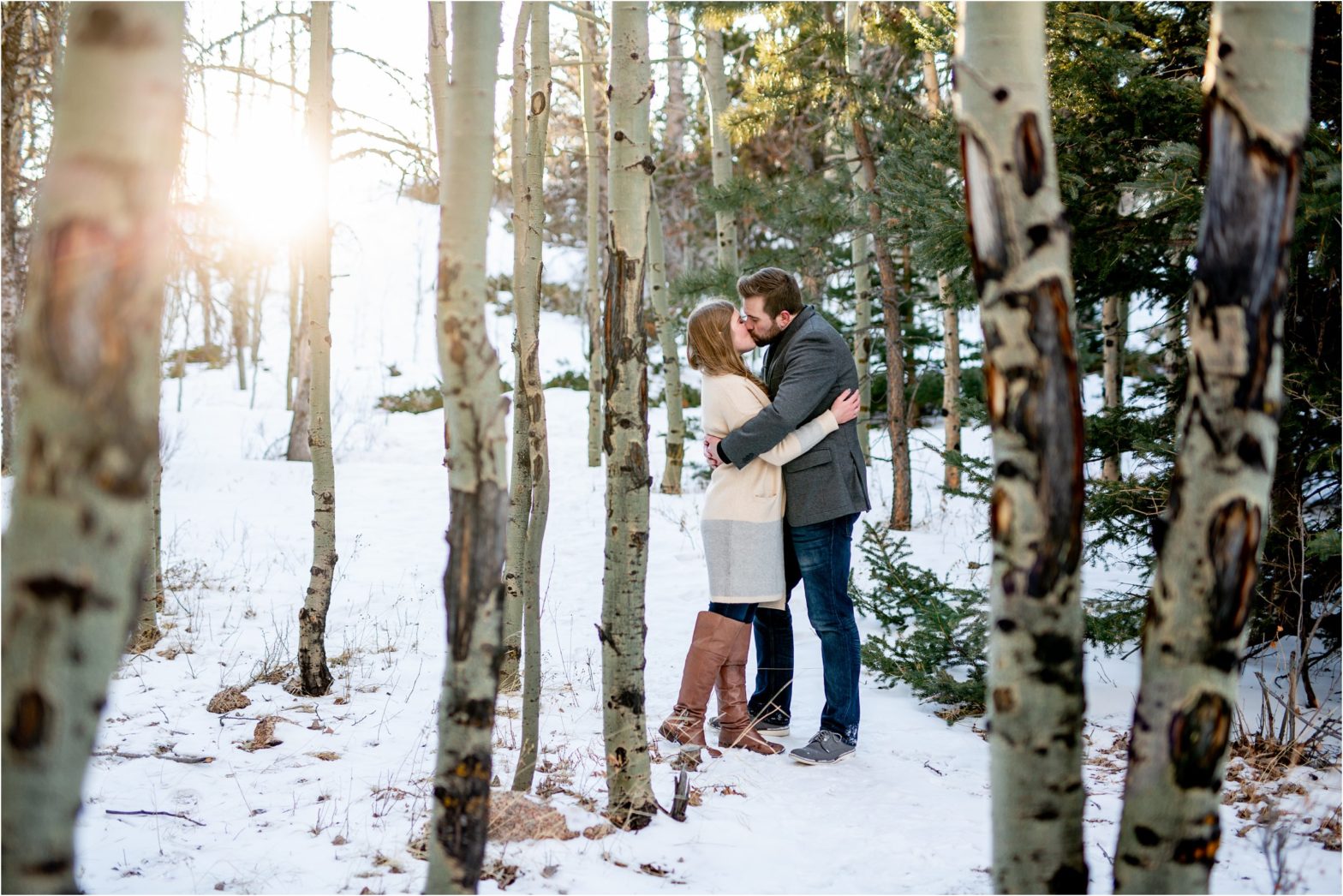 engaged couple snuggling in the snow with trees in the background