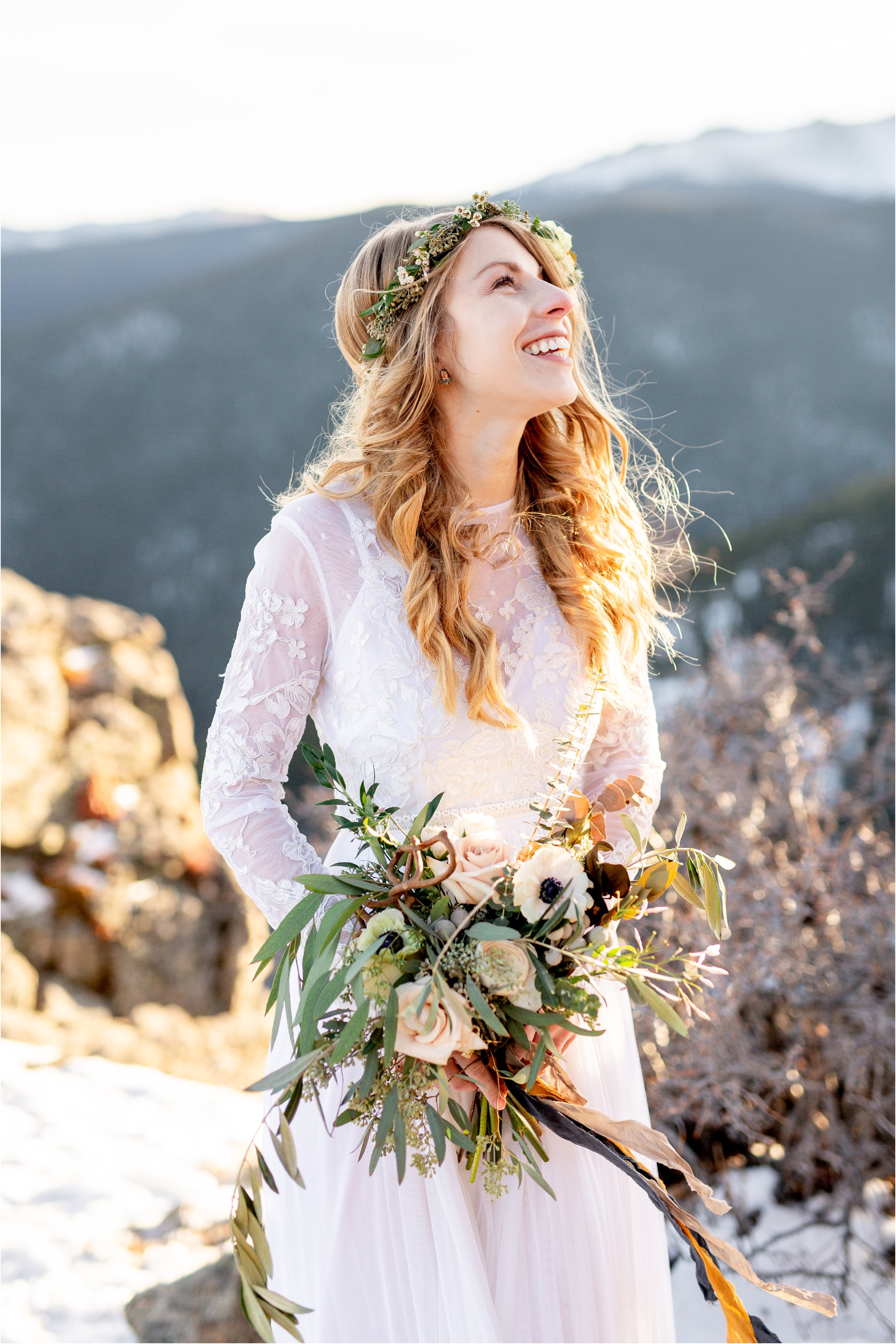 Bride standing along on mountain top with large bouquet and flower crown looking up