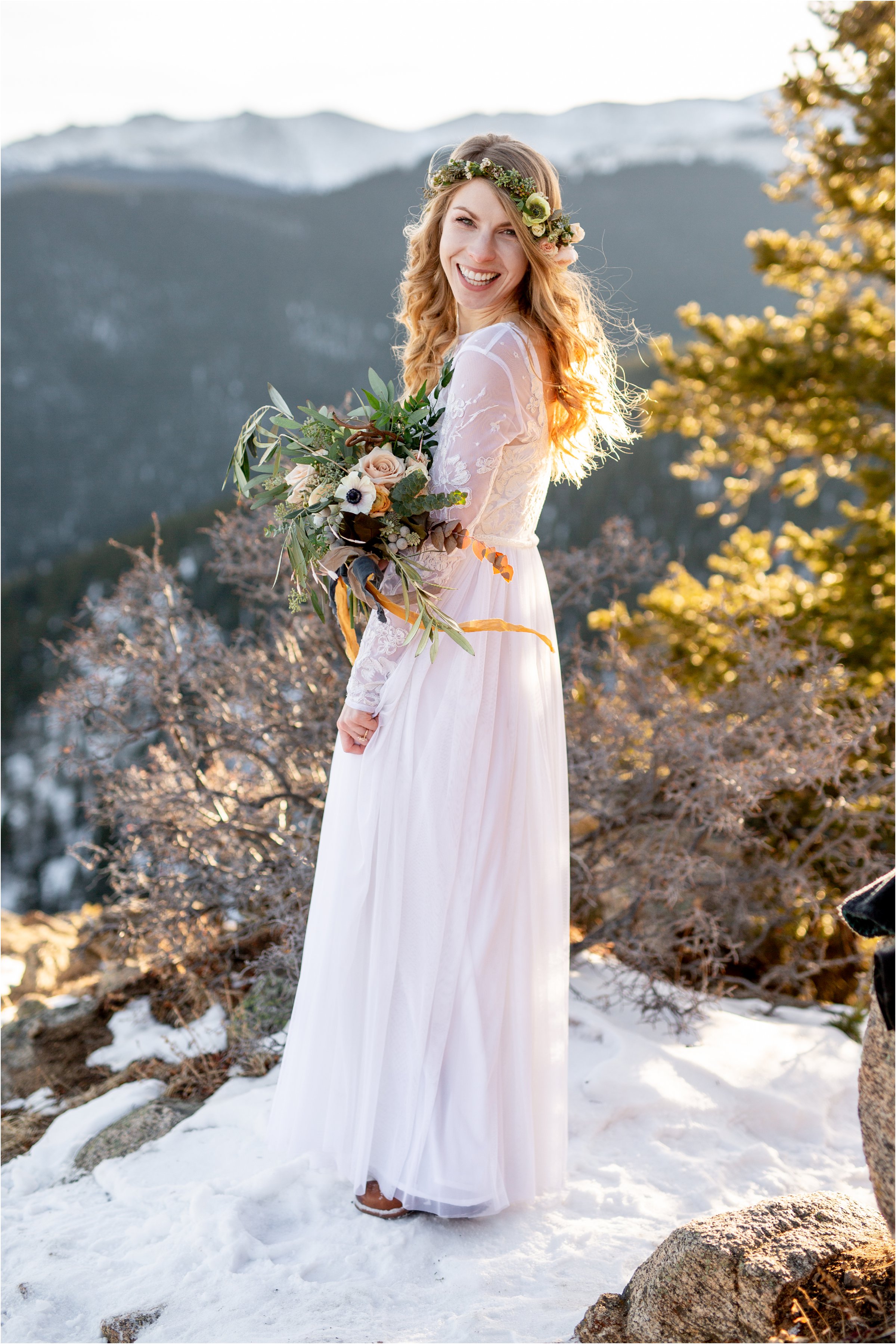 Bride standing alone with bouquet and flower crown, looking at camera with mountains in the background