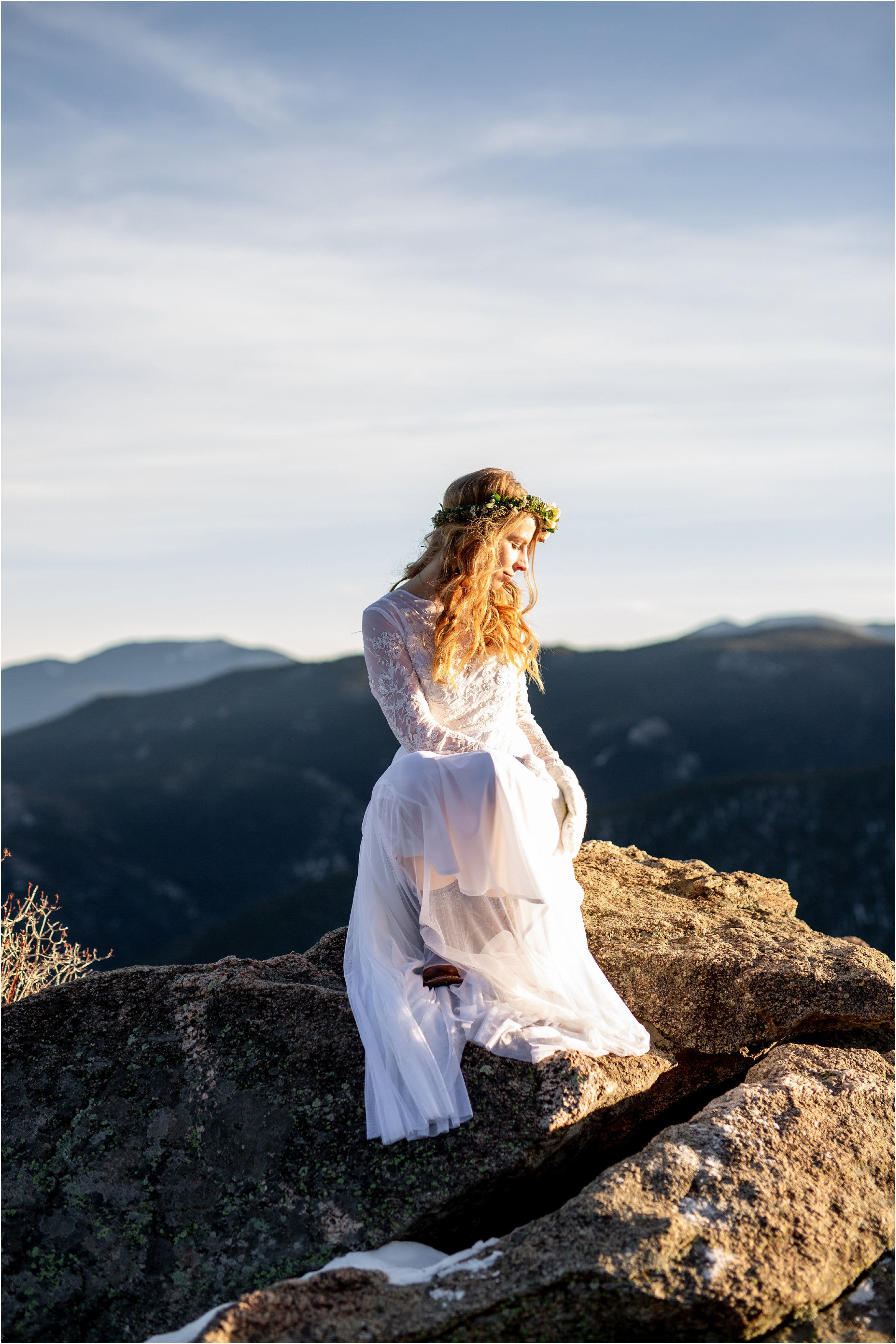 Bride sitting alone on mountain top in wedding dress with blue sky in the background during her Denver Elopement