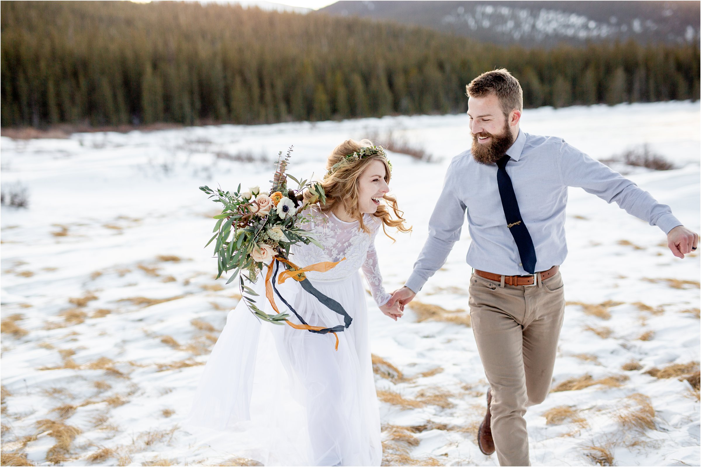 Couple in wedding attire running through a snowy field together