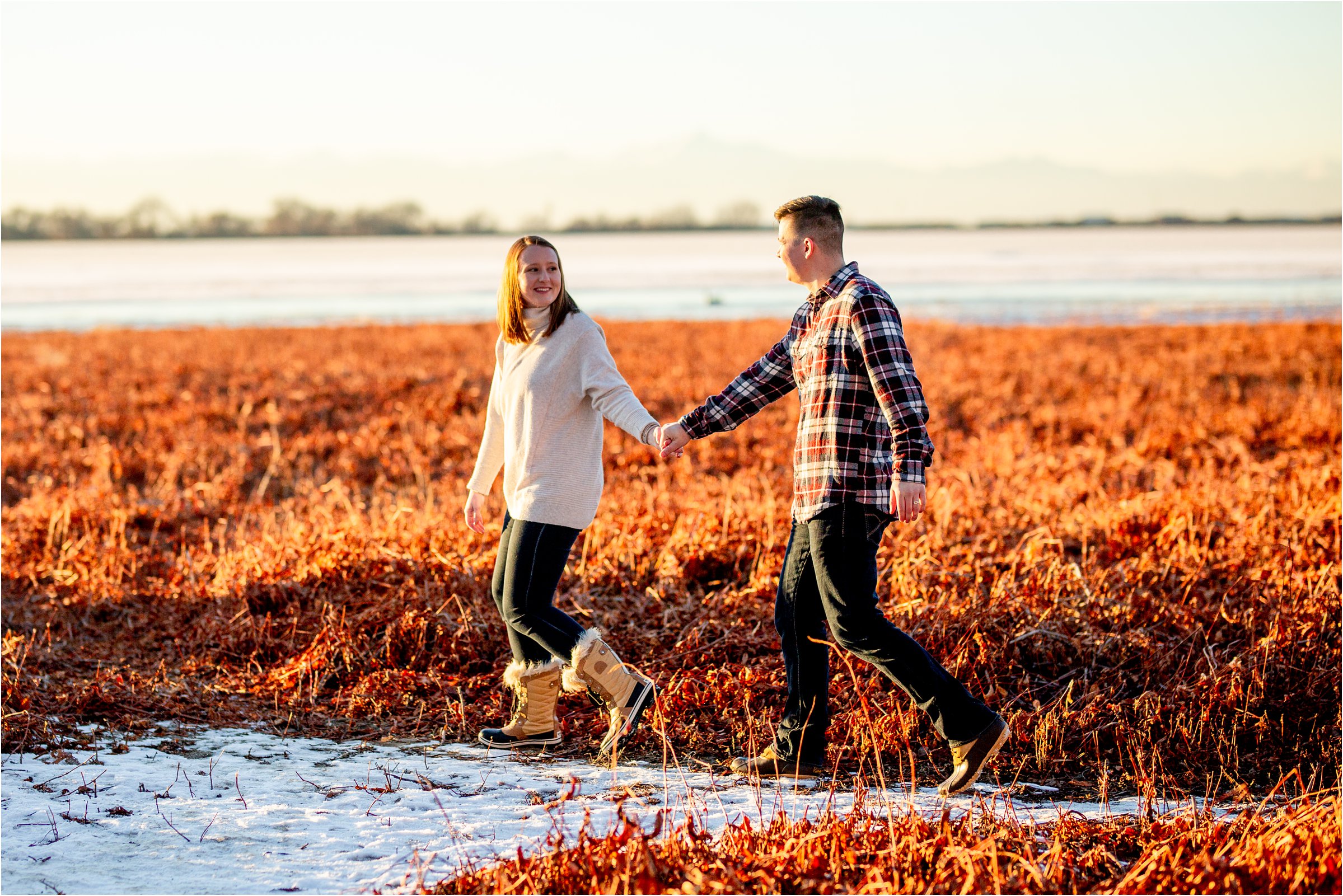 married couple walking through a field with patches of snow with barr lake in the background