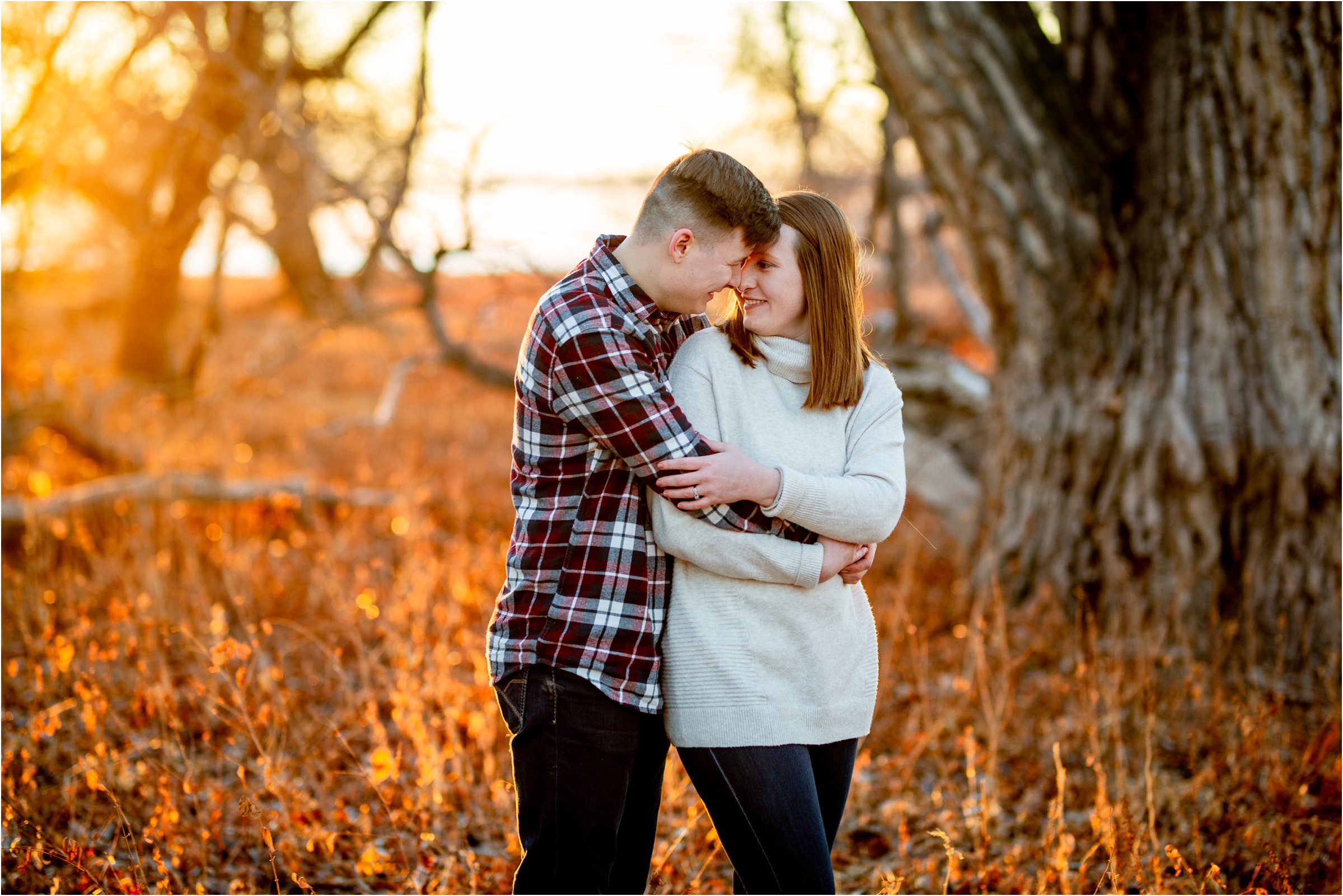 married couple snuggling in a field with sun shining bright orange through the backdrop