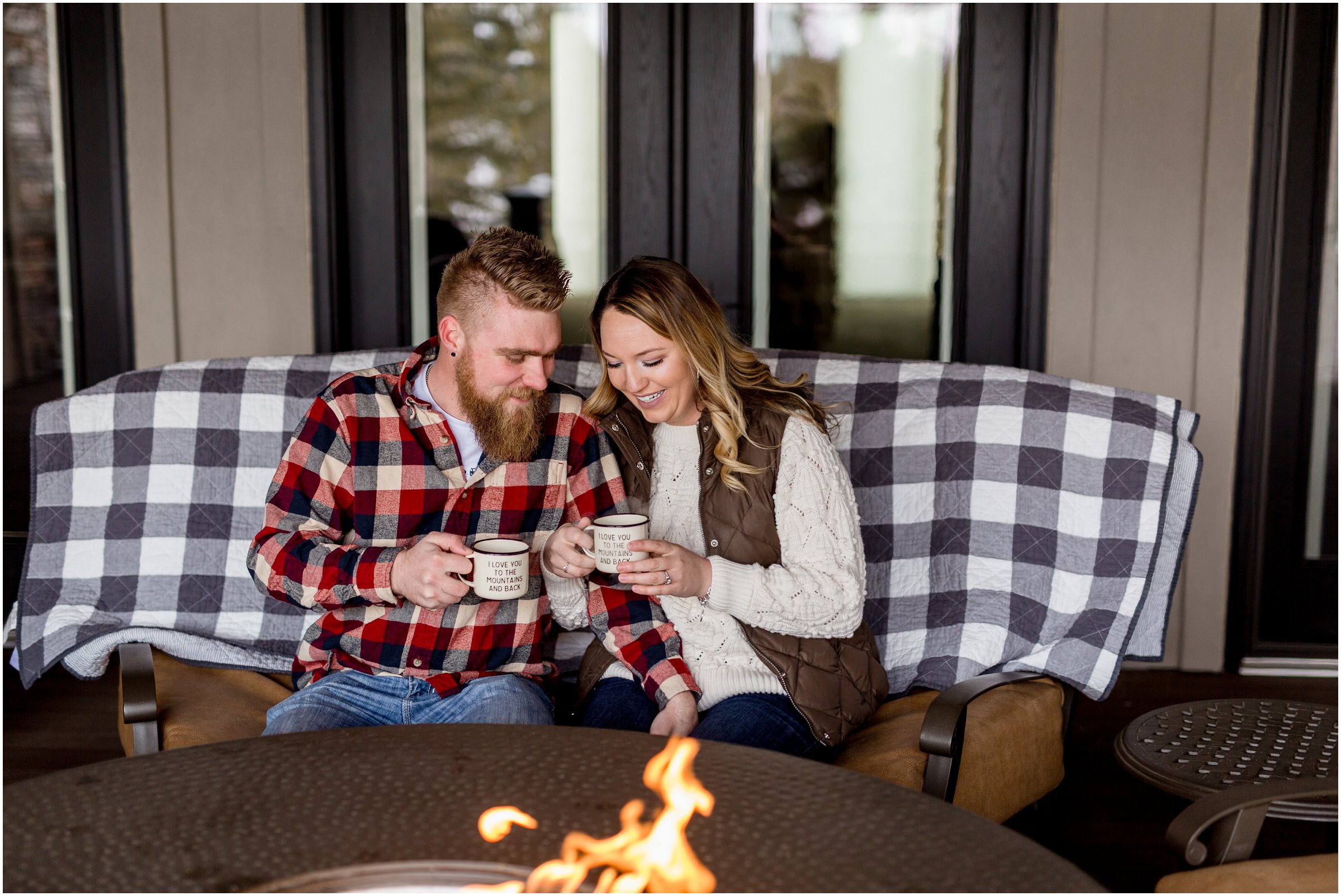 bride and groom sit by a fire with mugs that read I love you to the mountains and back