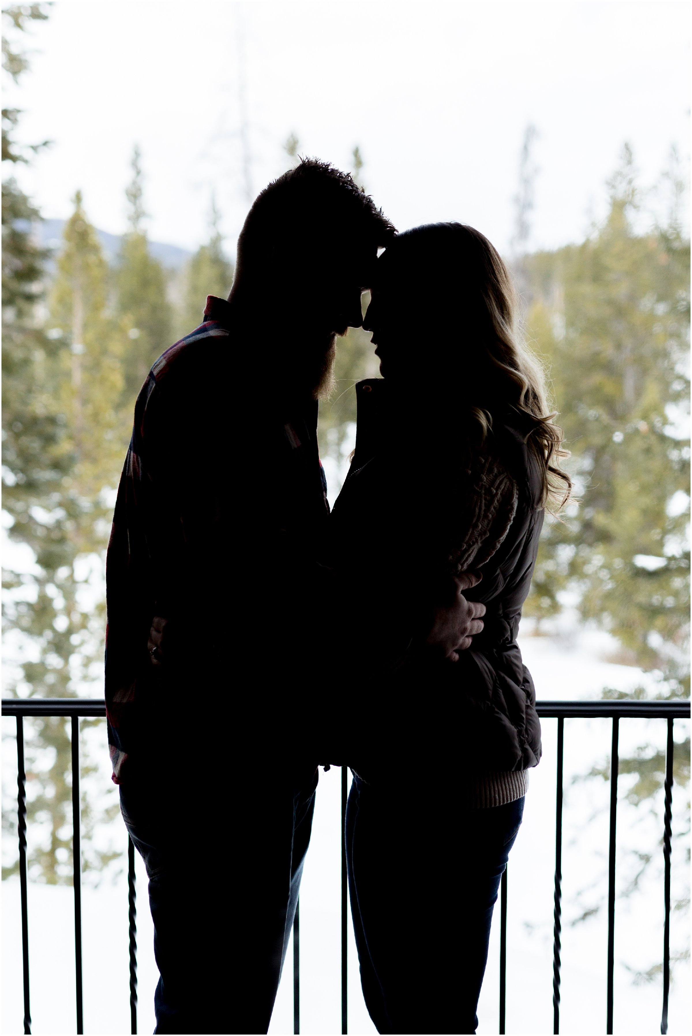 silhouette of a man and woman standing face to face with trees and snow in the background