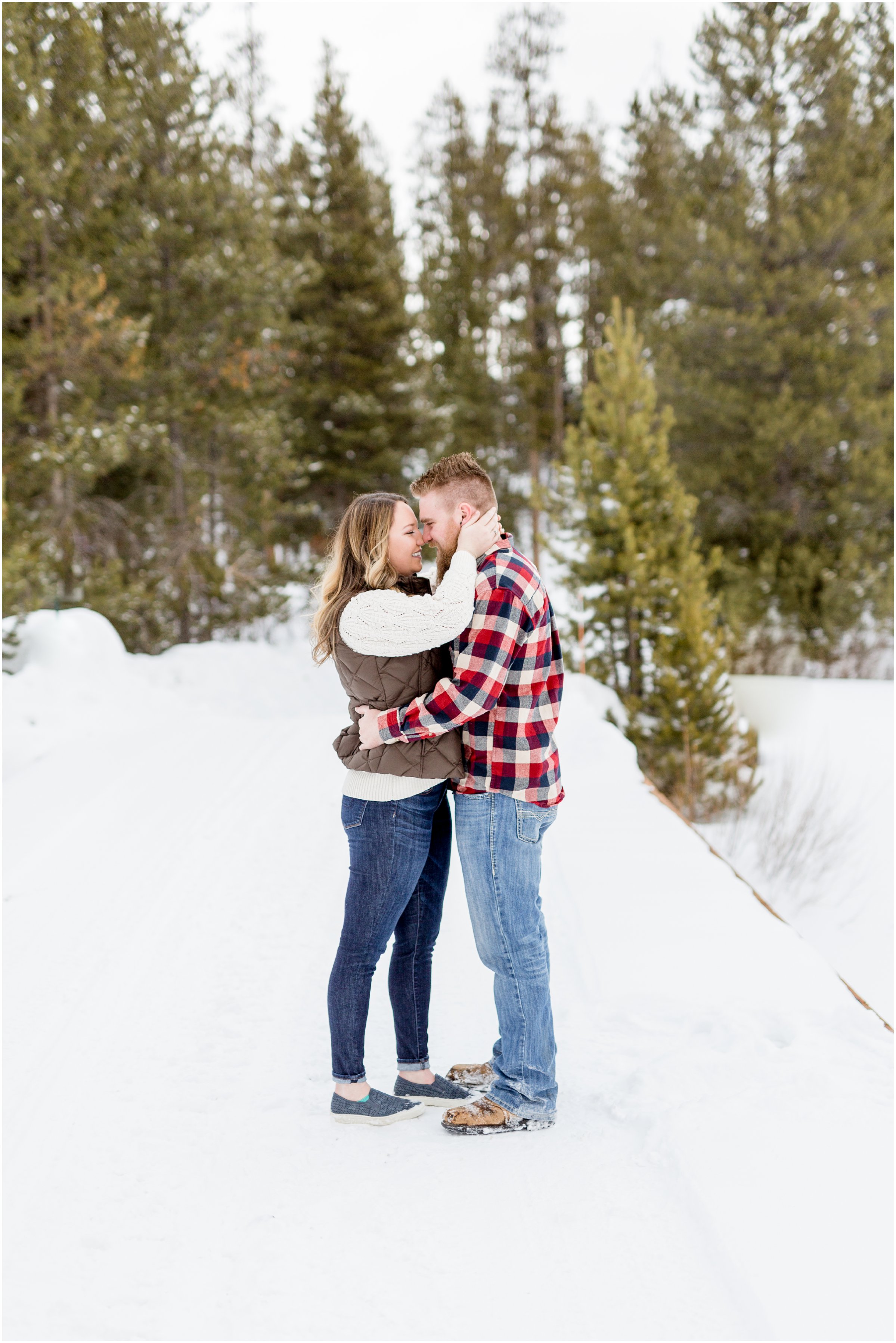 Man and woman stand face to face with snow on the ground and green trees in the background