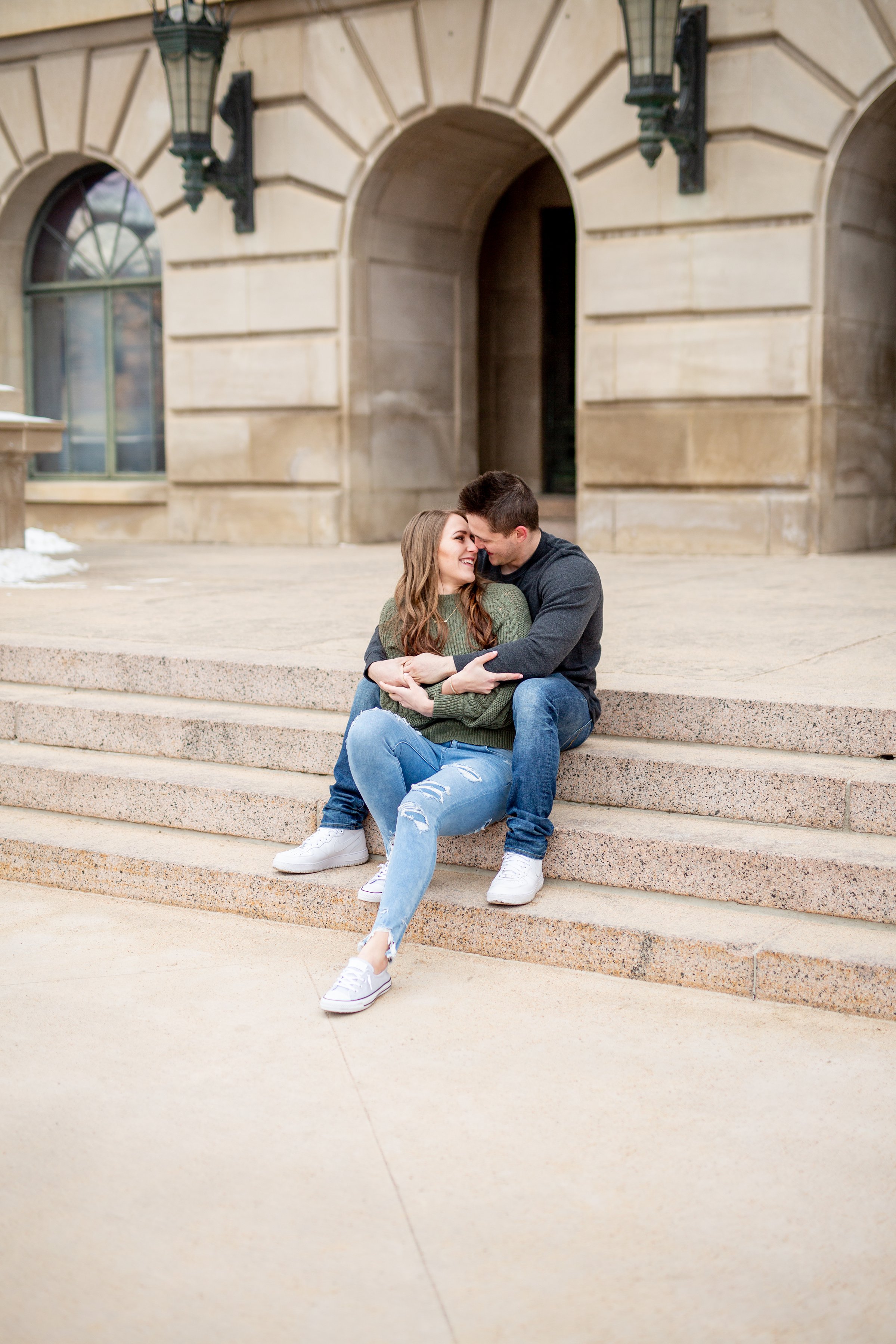 engaged couple snuggling on stairs in front of building with arched architecture for their fort collins engagement session
