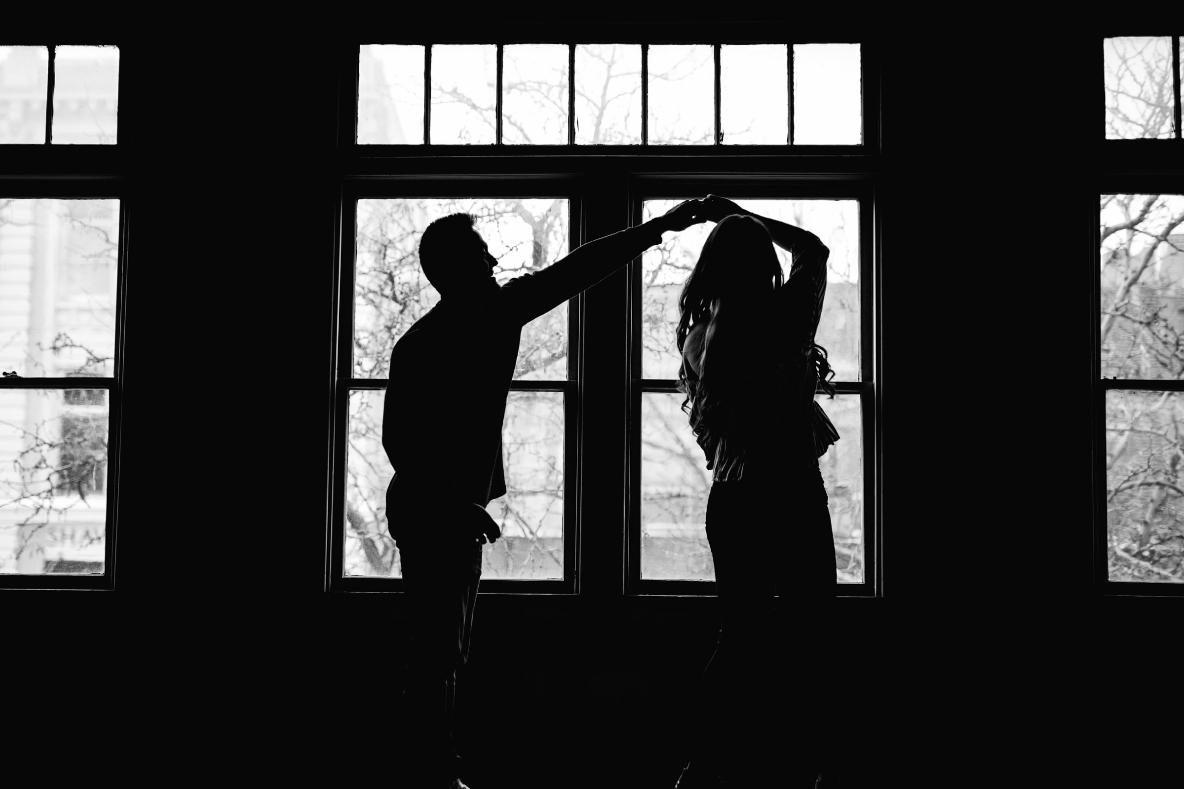 silhouettes of fort collins engaged couple dancing in front of a window in black and white