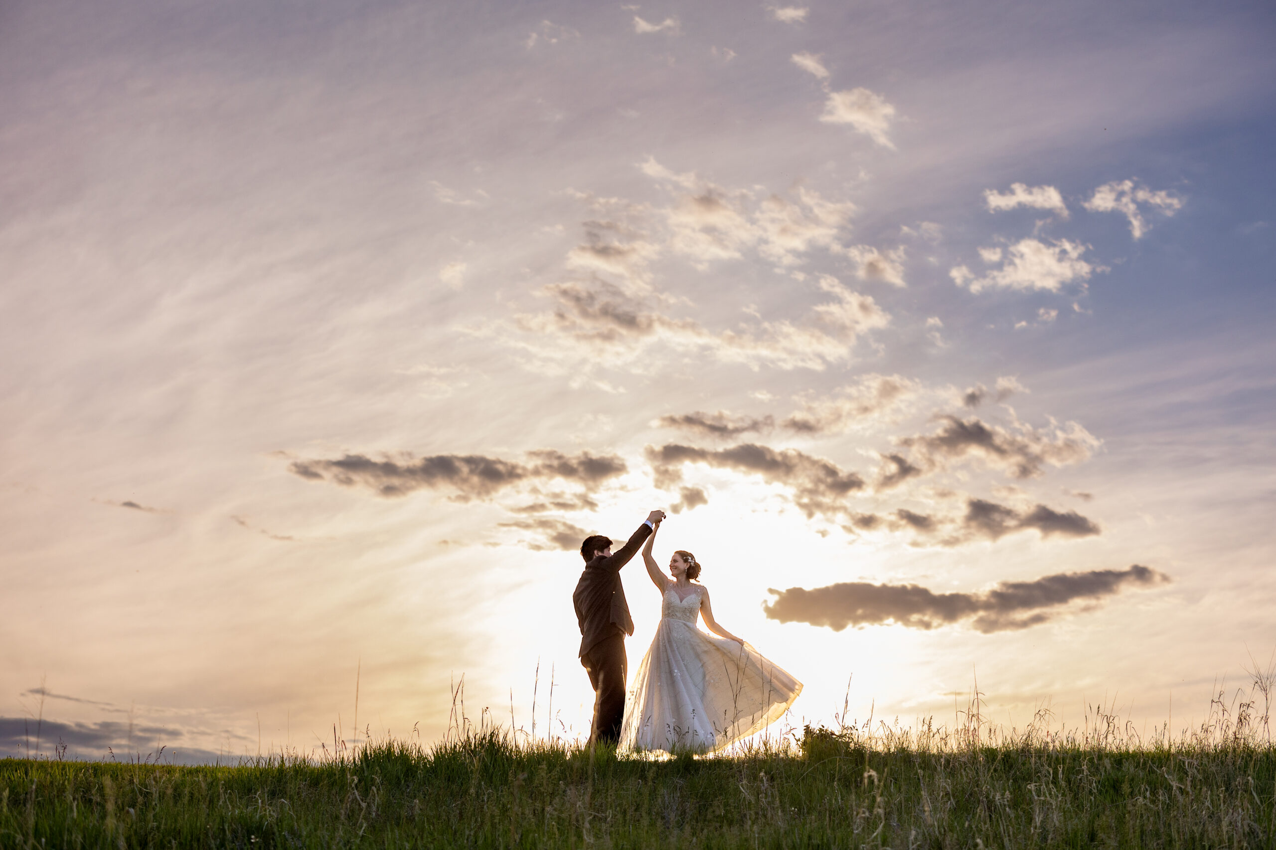 Wedding at Brader County Barn near Hastings Nebraska. Couple is silhouetted against and sunset with clouds